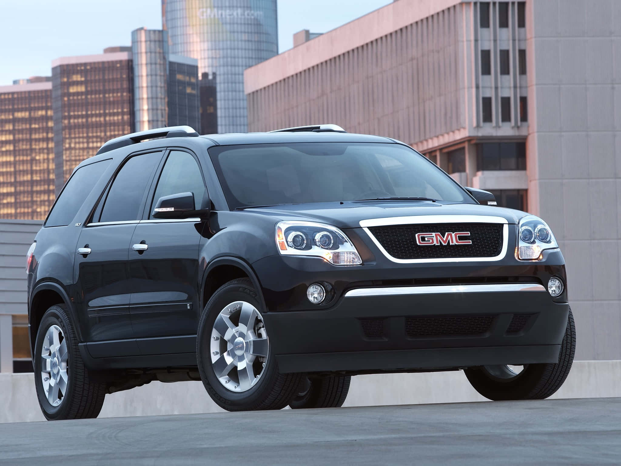 Gmc Acadia 桌布 壁紙 — 一輛時尚的黑色GMC SUV停放在都市屋頂，現代摩天大樓在傍晚燈光中閃耀。