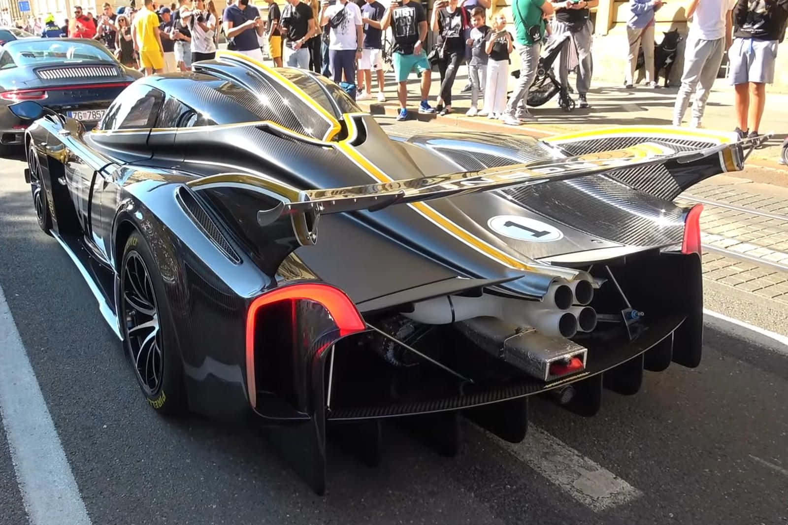 Pagani Zonda C12 Roadster 桌布 壁紙 — 一輛時尚的黑色和黃色超級跑車，配備四出排氣管和碳纖維細節，停在陽光明媚的街道上，周圍有觀眾。