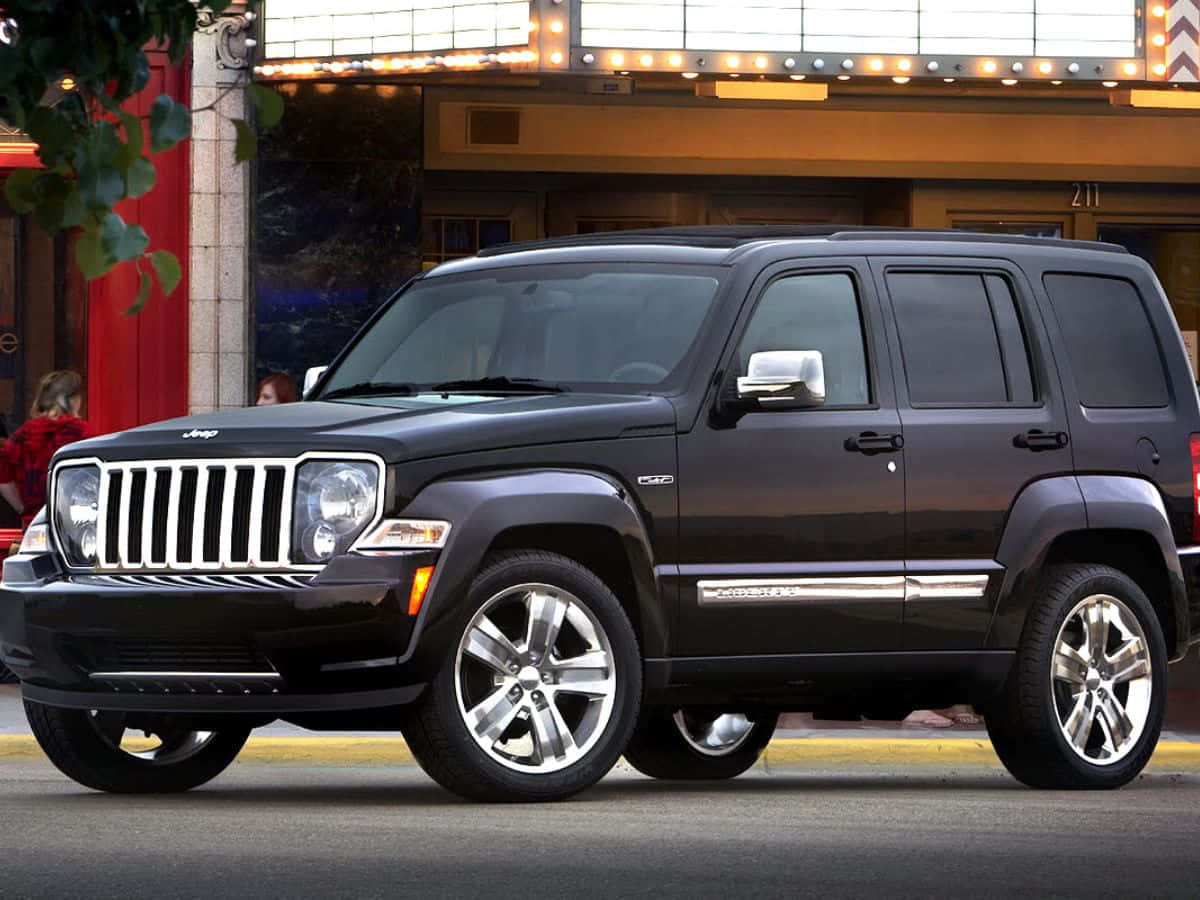 Jeep Liberty 桌布 壁紙 — 一輛時尚的黑色Jeep Patriot SUV停泊在繁華街道上，前方是燈光明亮的劇院外牆。