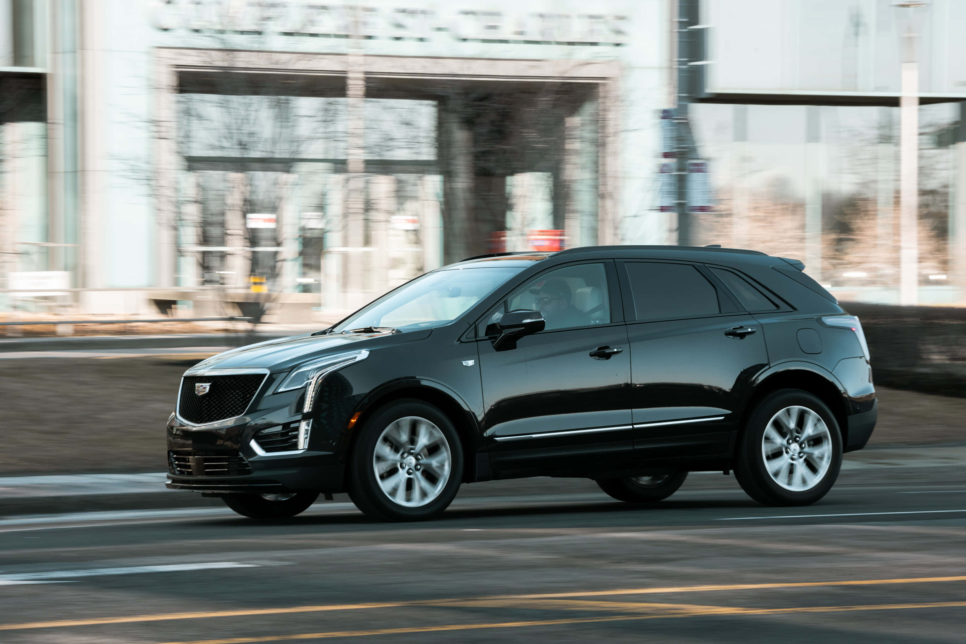 Cadillac Xt5 桌布 壁紙 — 一輛時尚的黑色凱迪拉克SUV在城市街道上行駛，背景建築物因動態模糊而變得模糊。