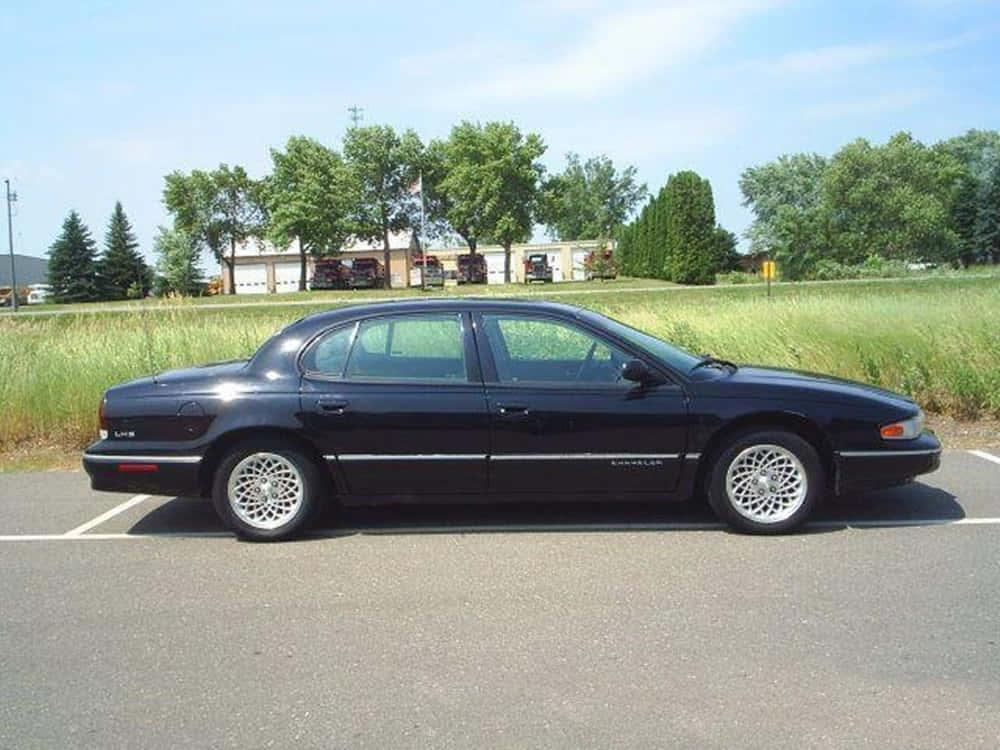 Chrysler Lhs 桌布 壁紙 — 一輛時尚的黑色克萊斯勒LHS轎車停放在陽光明媚的地方，後面有綠草和樹木。
