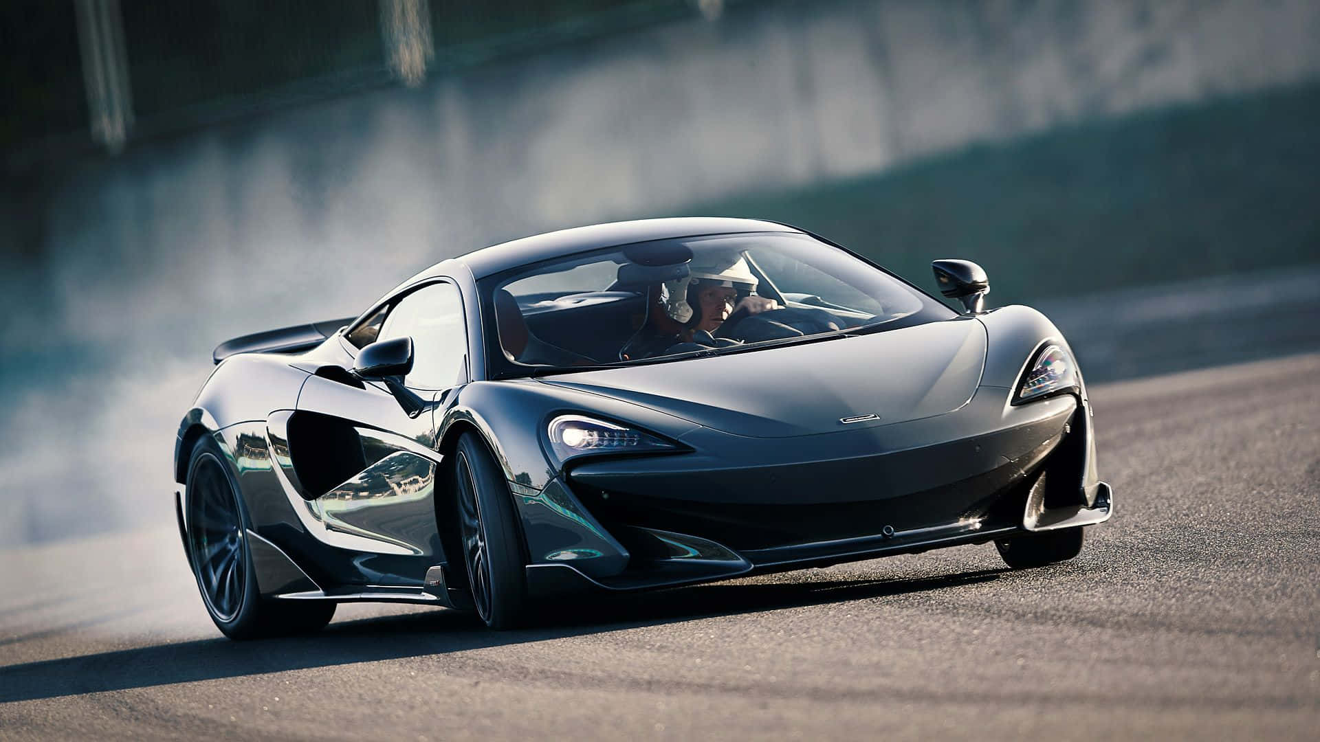 Mclaren 600lt 桌布 壁紙 — 一輛時尚的黑色McLaren跑車在賽道上飄移，輪胎在明亮的日光下冒出滾滾濃煙。