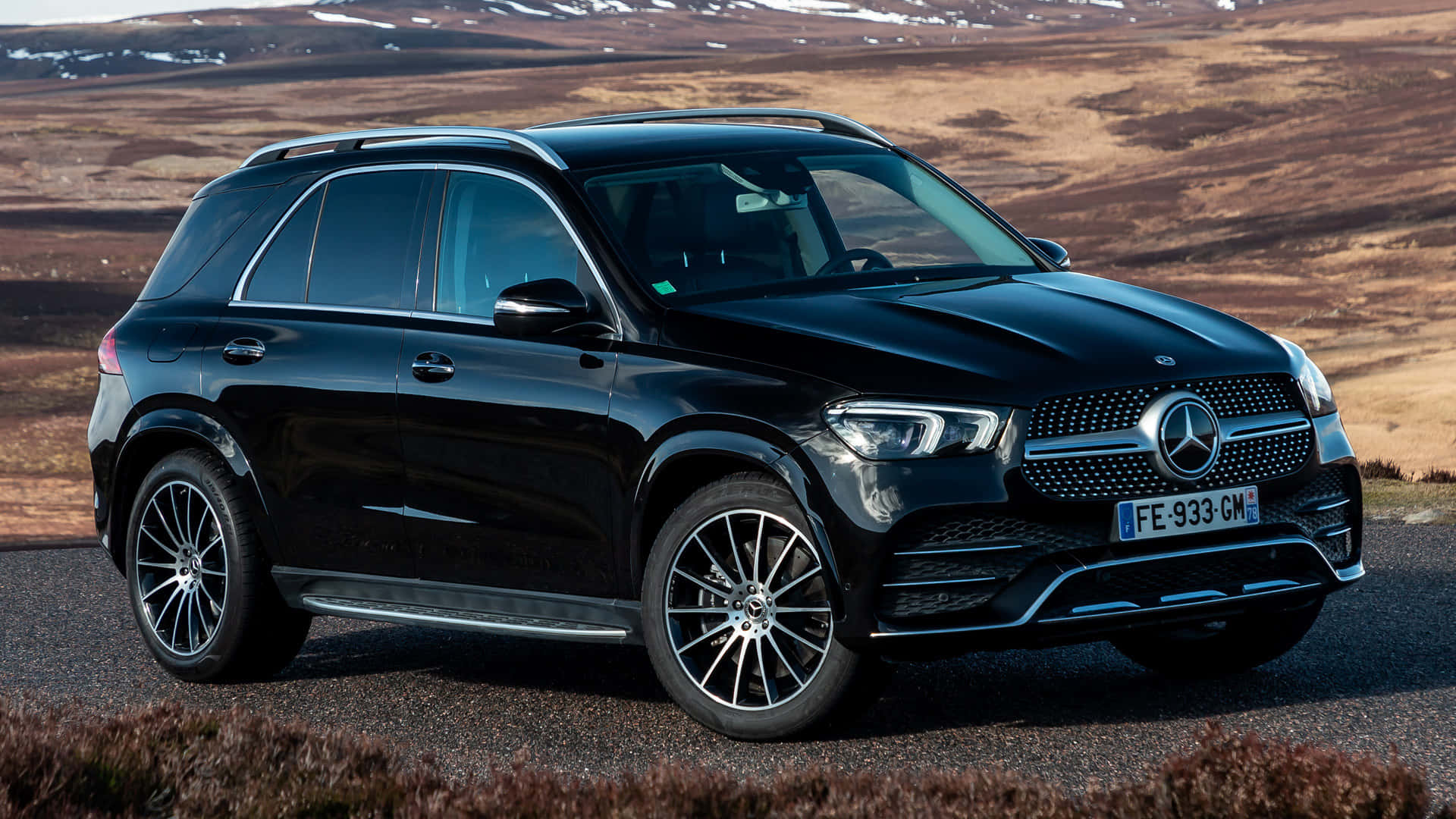Mercedes Benz Gle-class 桌布 壁紙 — 一輛時尚的黑色 Mercedes-Benz GLE SUV 停泊在碎石路上，背景是崎嶇的棕色和積雪的山脈。