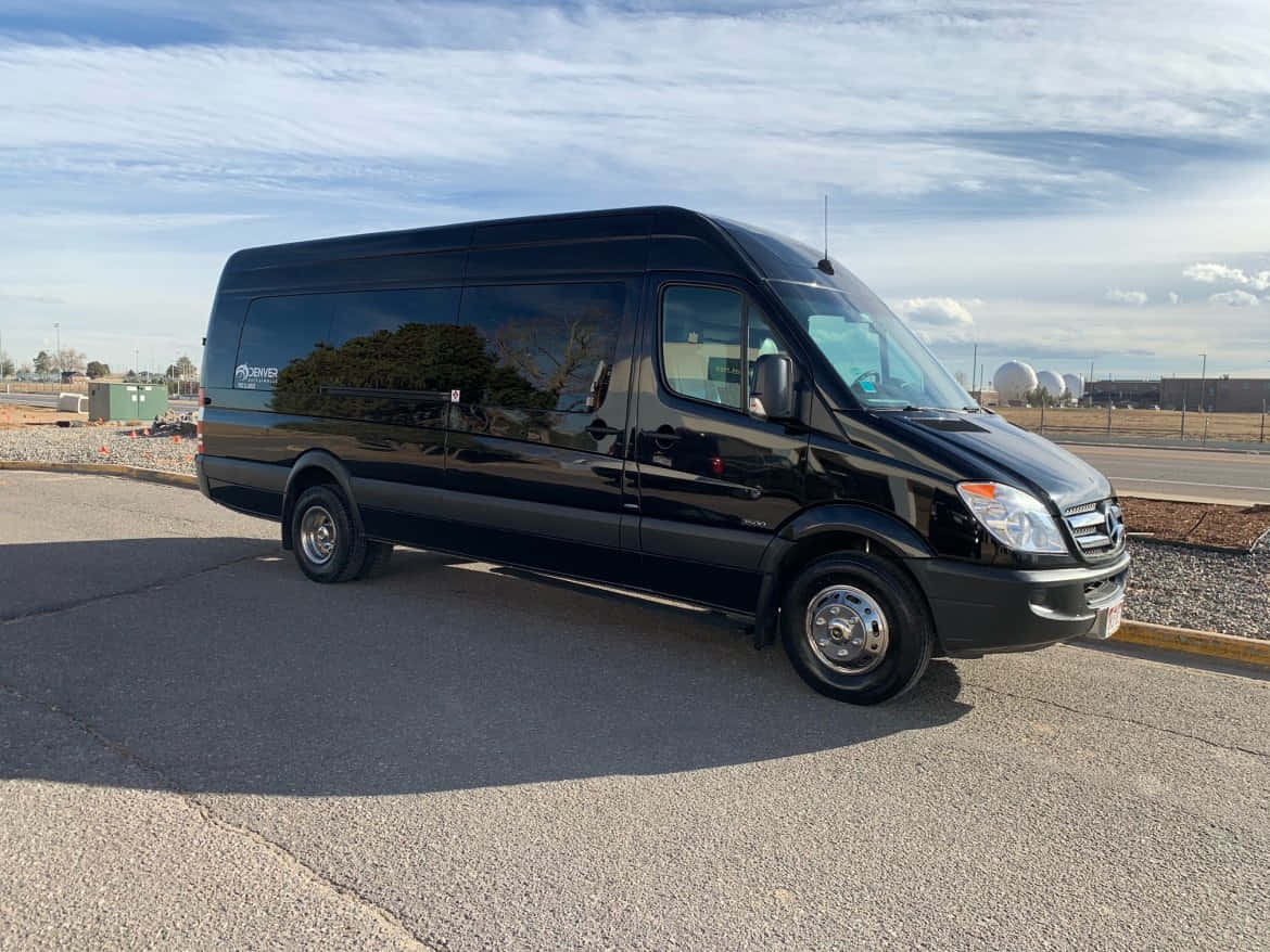 Mercedes Benz Sprinter 桌布 壁紙 — 一輛時尚的黑色 Mercedes-Benz Sprinter 客貨車停在瀝青路面上，天空部分多雲，背景有遠處的圓頂建築。