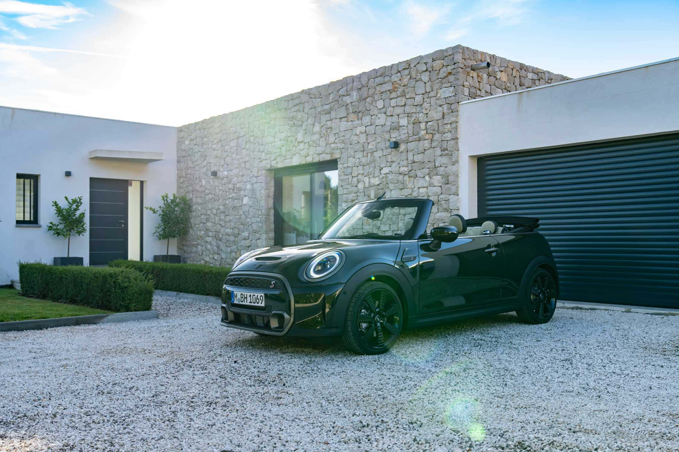 Mini Cooper S Convertible 桌布 壁紙 — 一輛時尚的黑色MINI敞篷車停在碎石車道上，前面是現代石頭和白色房屋，帶有太陽眩光。