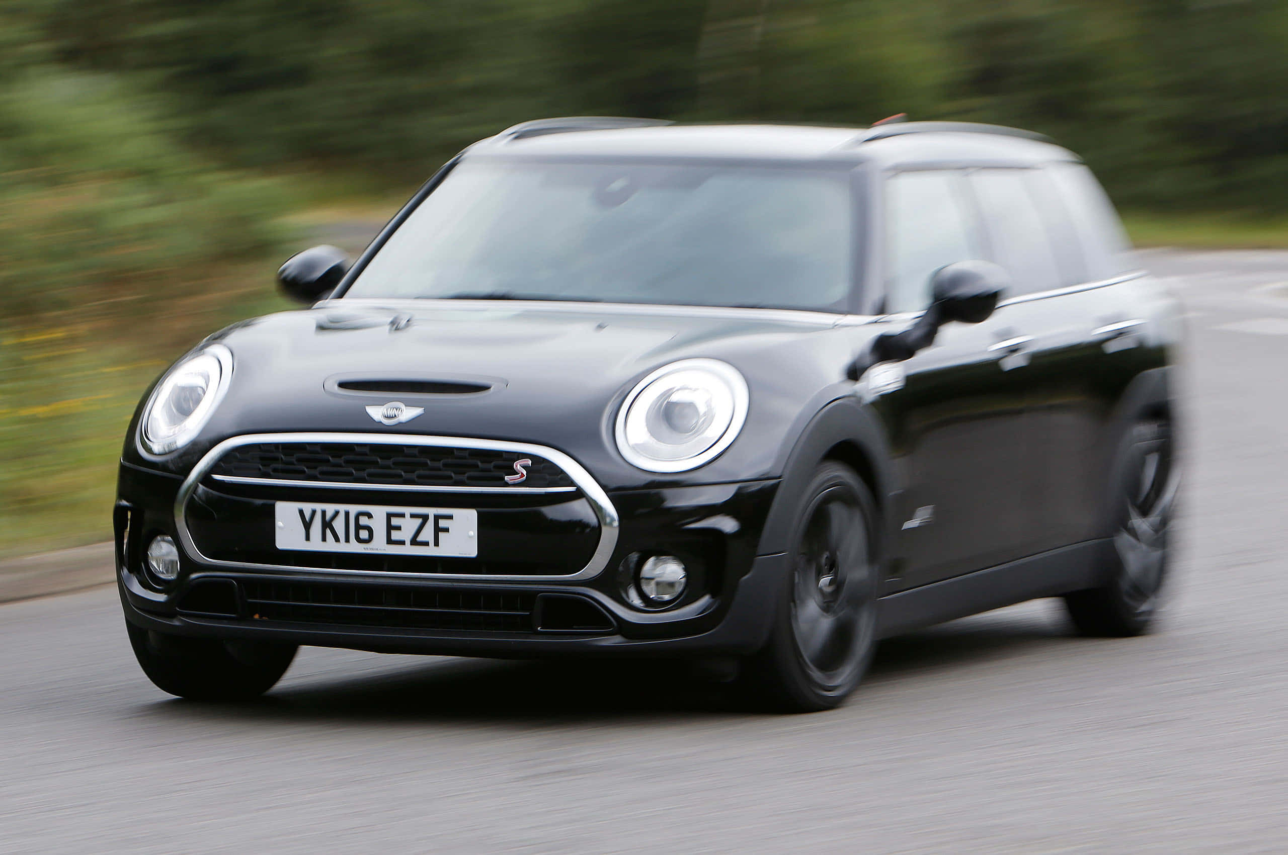 Mini Cooper S Clubman All4 桌布 壁紙 — 一輛時尚的黑色MINI Countryman S在道路上奔馳，背景是模糊的綠色植物。