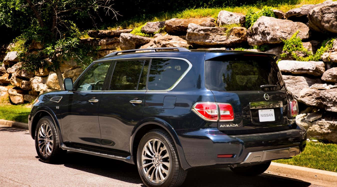 Nissan Armada 桌布 壁紙 — 一輛時尚的黑色日產Armada SUV停放在鋪砌道路上，旁邊是陽光照射的石牆和綠草。