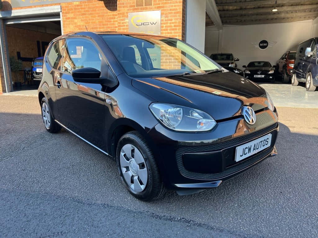  壁紙 — 一輛時尚的黑色Volkswagen up！停在磚砌車庫前，車庫內可見其他車輛。