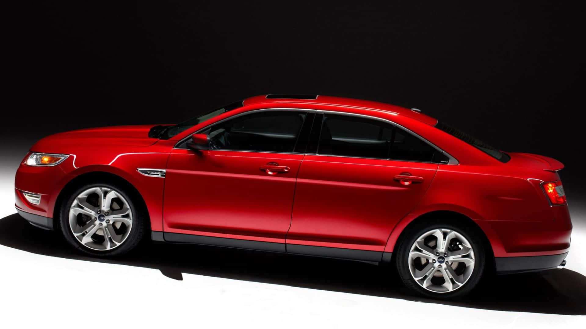 Ford Taurus 桌布 壁紙 — 一輛時尚的紅色轎車在攝影棚燈光下，在黑白背景中閃閃發光。