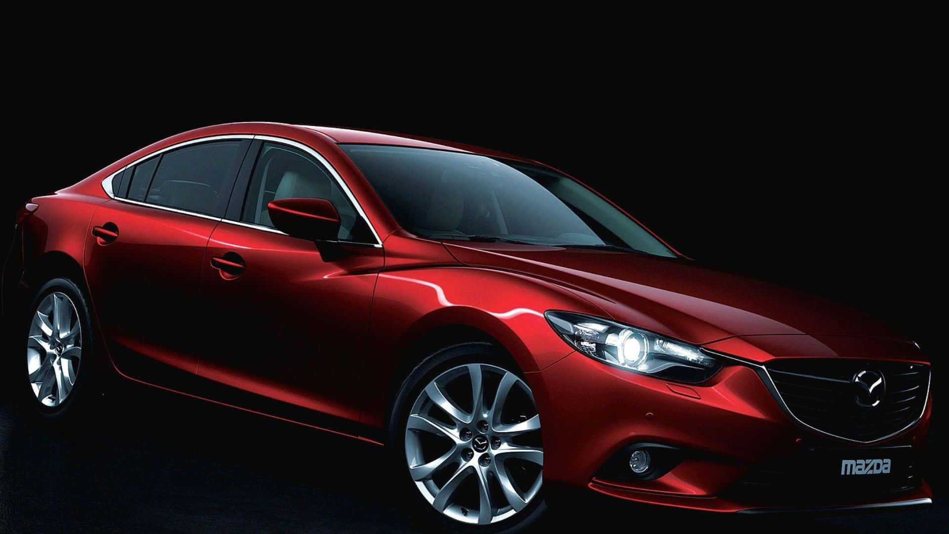 Mazda 6 桌布 壁紙 — 一輛時尚的紅色馬自達轎車在純黑色背景下於攝影棚燈光下閃耀，展示其空氣動力學曲線和拋光合金輪圈。