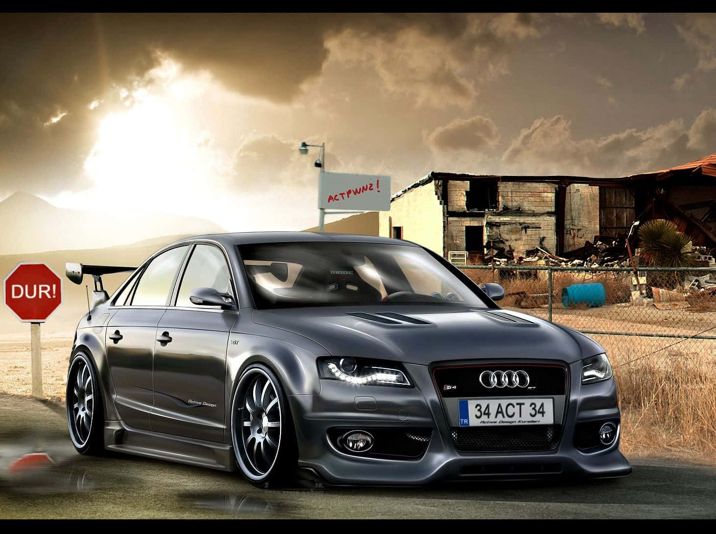 Audi S4 桌布 壁紙 — 一輛時尚的灰色奧迪轎車，配備定制輪圈和後擾流板，停在塵土飛揚的道路上，旁邊是一棟破舊的建築，背景是戲劇性的日落天空。