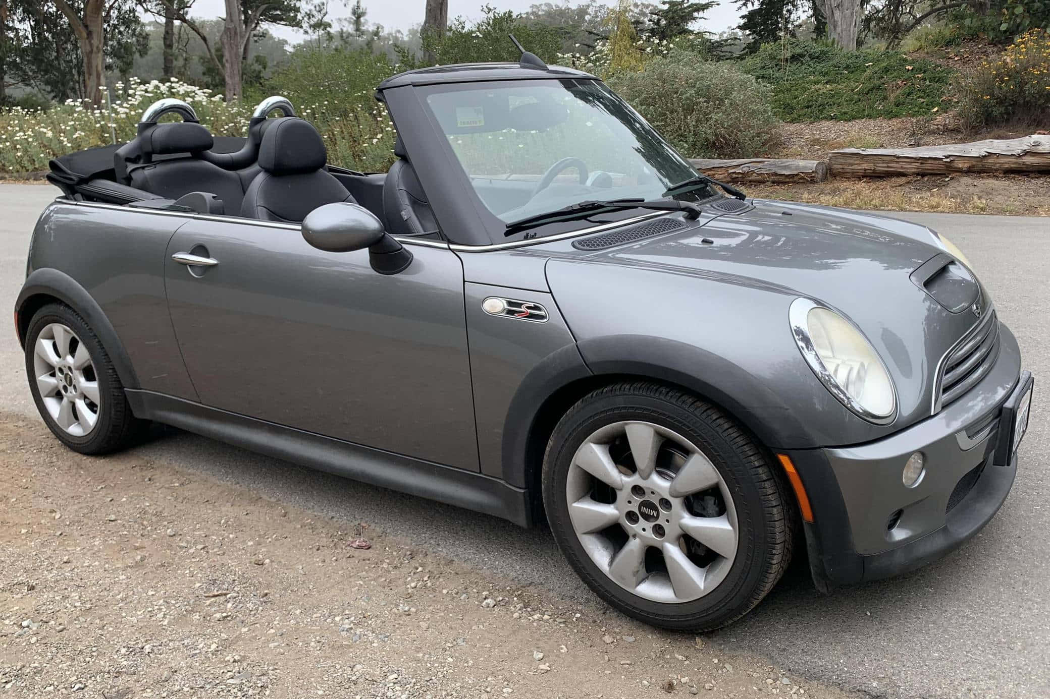 Mini Cooper Convertible 桌布 壁紙 — 一輛時尚的灰色敞篷跑車停泊在碎石路上，背景有樹木和野花。
