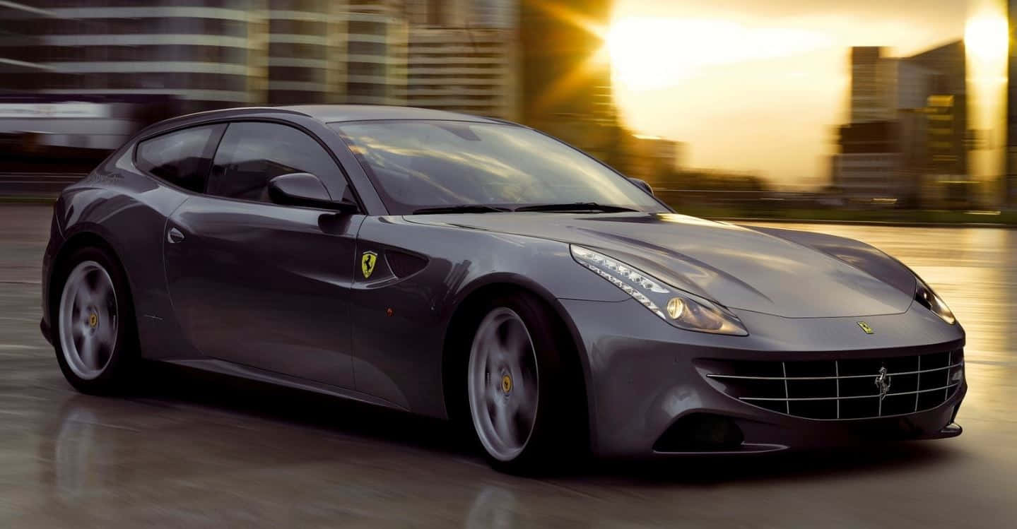 Ferrari Ff 桌布 壁紙 — 一輛時尚的灰色法拉利跑車在金色日落時分穿過模糊的城市景觀。