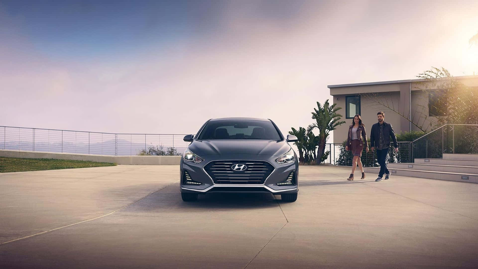 Hyundai Sonata 桌布 壁紙 — 一輛時尚的灰色Hyundai房車停放在現代化車道上，附近有一對夫婦在黃金時段於當代房屋旁散步。