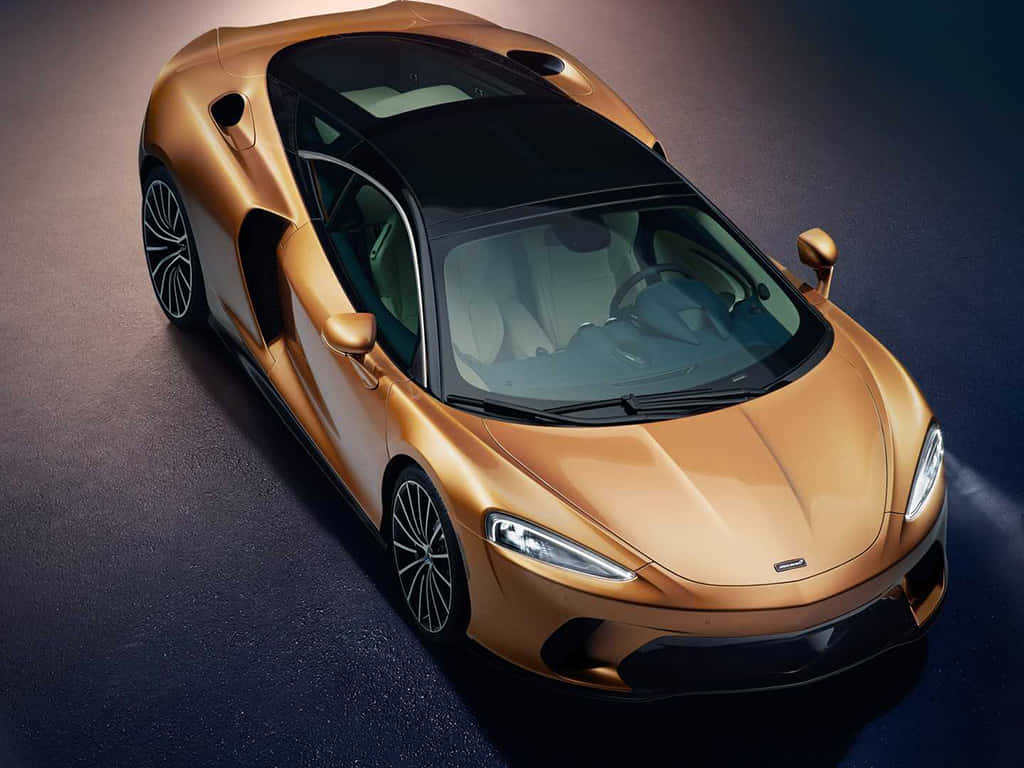 Mclaren Gt 桌布 壁紙 — 一輛時尚的金色跑車，帶有黑色飾邊和未來感設計，在攝影棚燈光下閃耀。