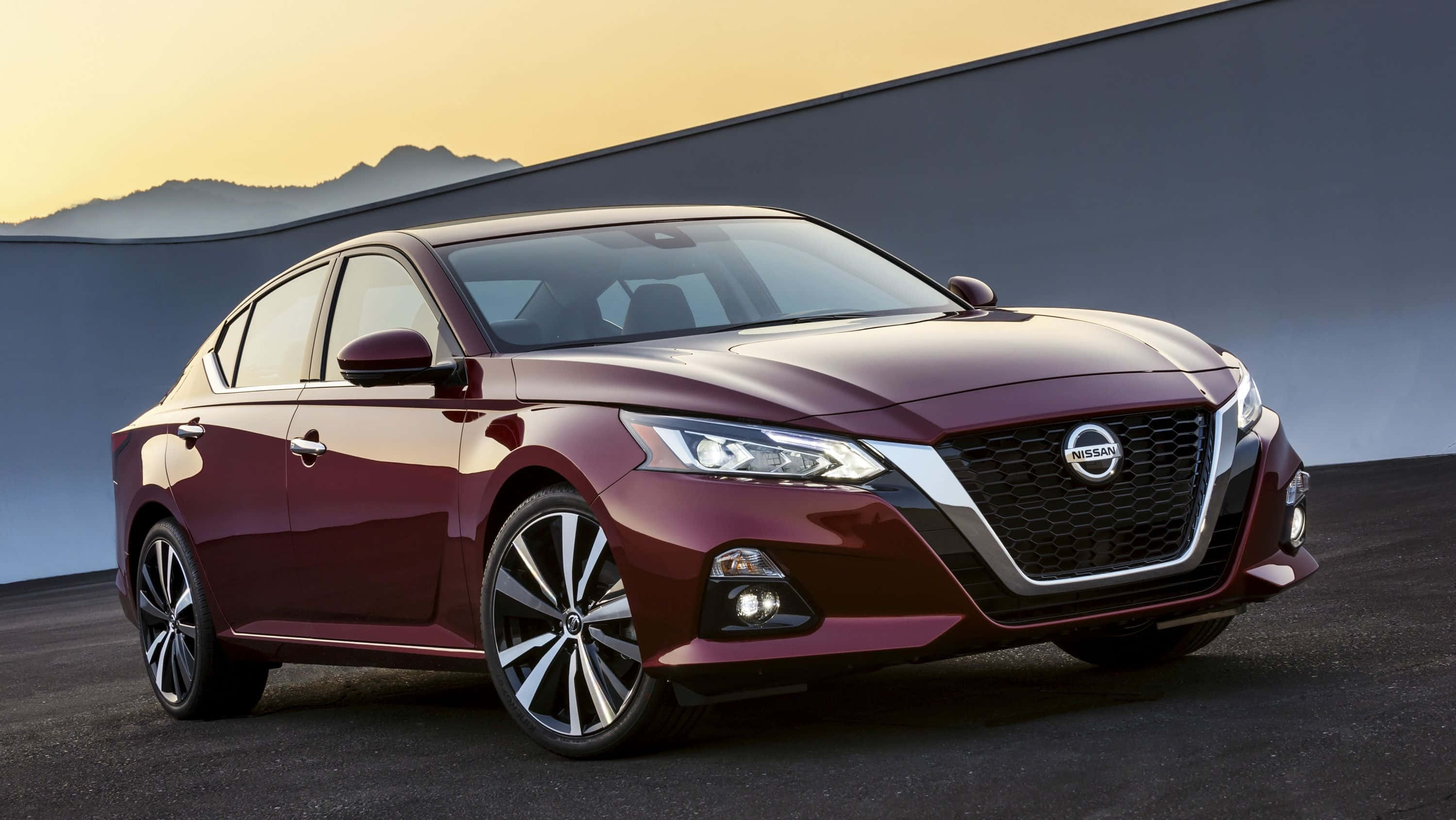 Nissan Altima 桌布 壁紙 — 一輛時尚的酒紅色日產轎車在金色夕陽下閃耀，背景是簡約的山脈。
