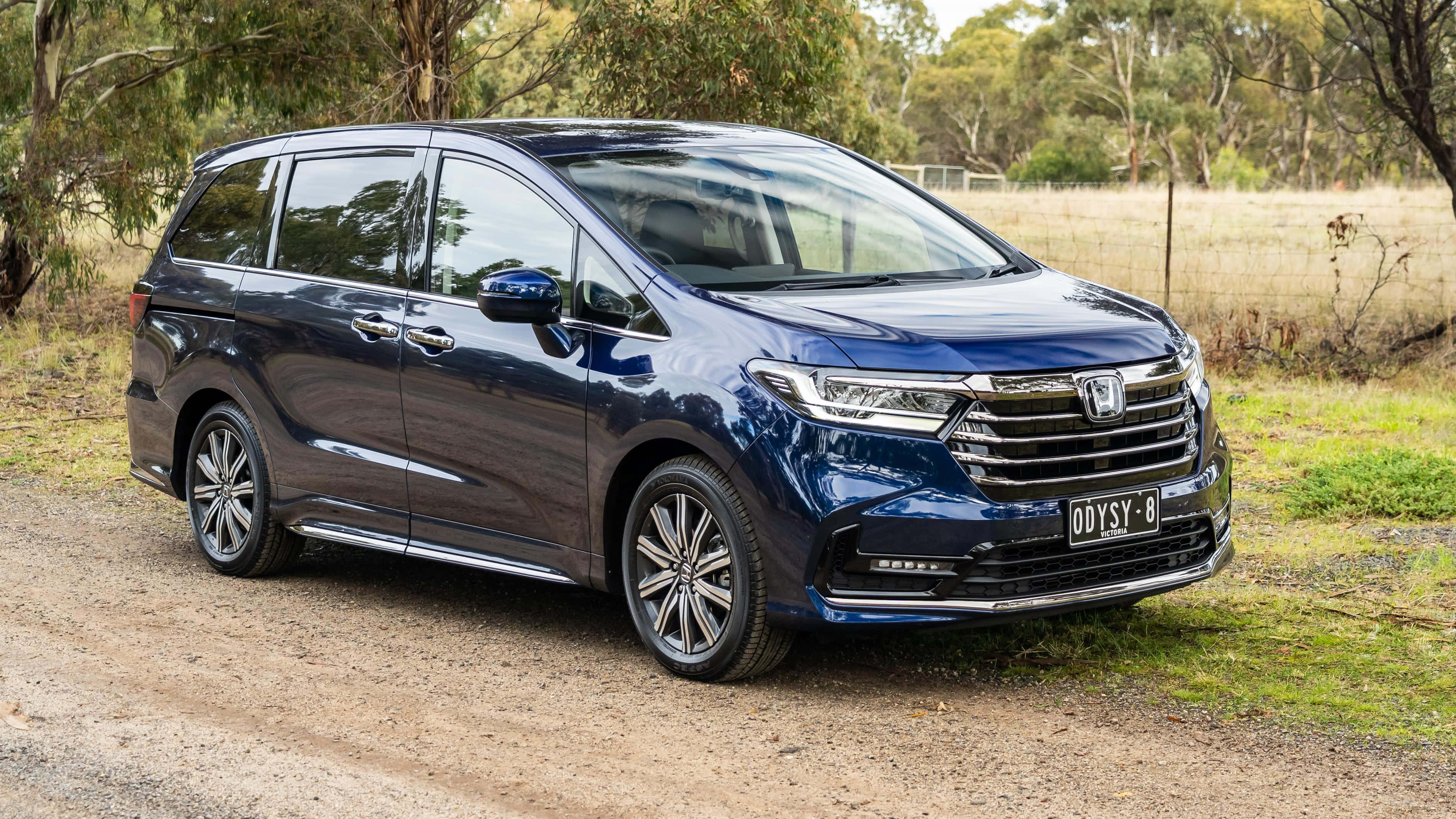 Honda Odyssey 桌布 壁紙 — 一輛時尚的藍色本田Odyssey小型貨車停泊在泥路上，周圍環繞著樹木和草地。