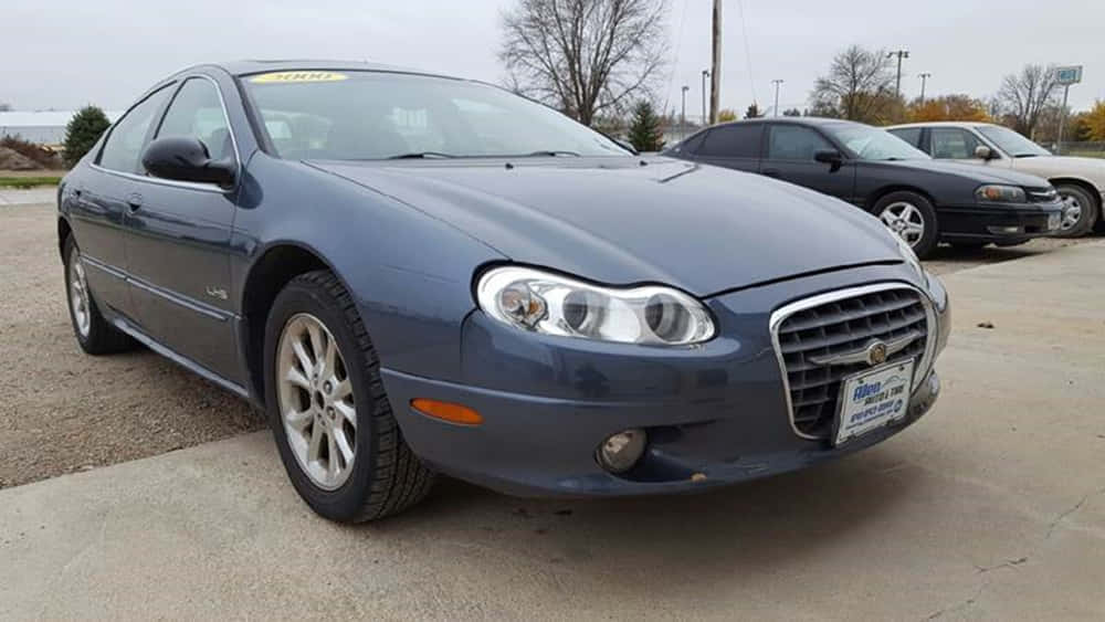 Chrysler Lhs 桌布 壁紙 — 一輛時尚的藍色 Chrysler 轎車停在碎石停車場，背景有光禿的樹木和陰天。