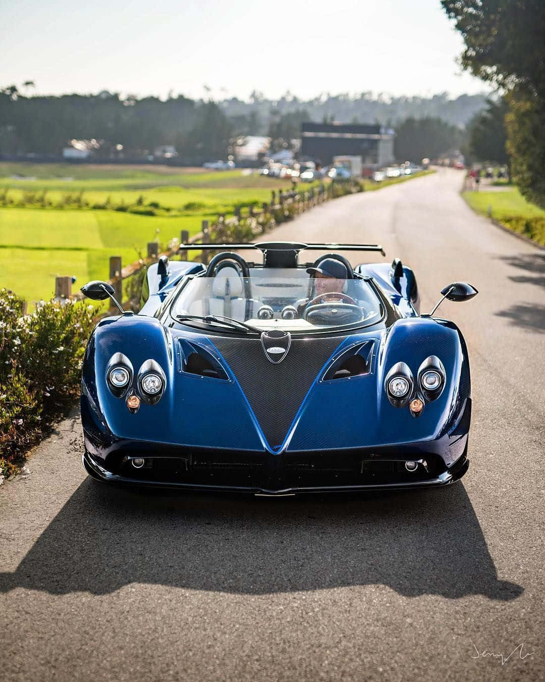 Pagani Zonda Hp Barchetta 桌布 壁紙 — 一輛時尚的藍色Pagani Huayra敞篷跑車停泊在陽光明媚的鄉村道路上，背景是綠色的田野和樹木。