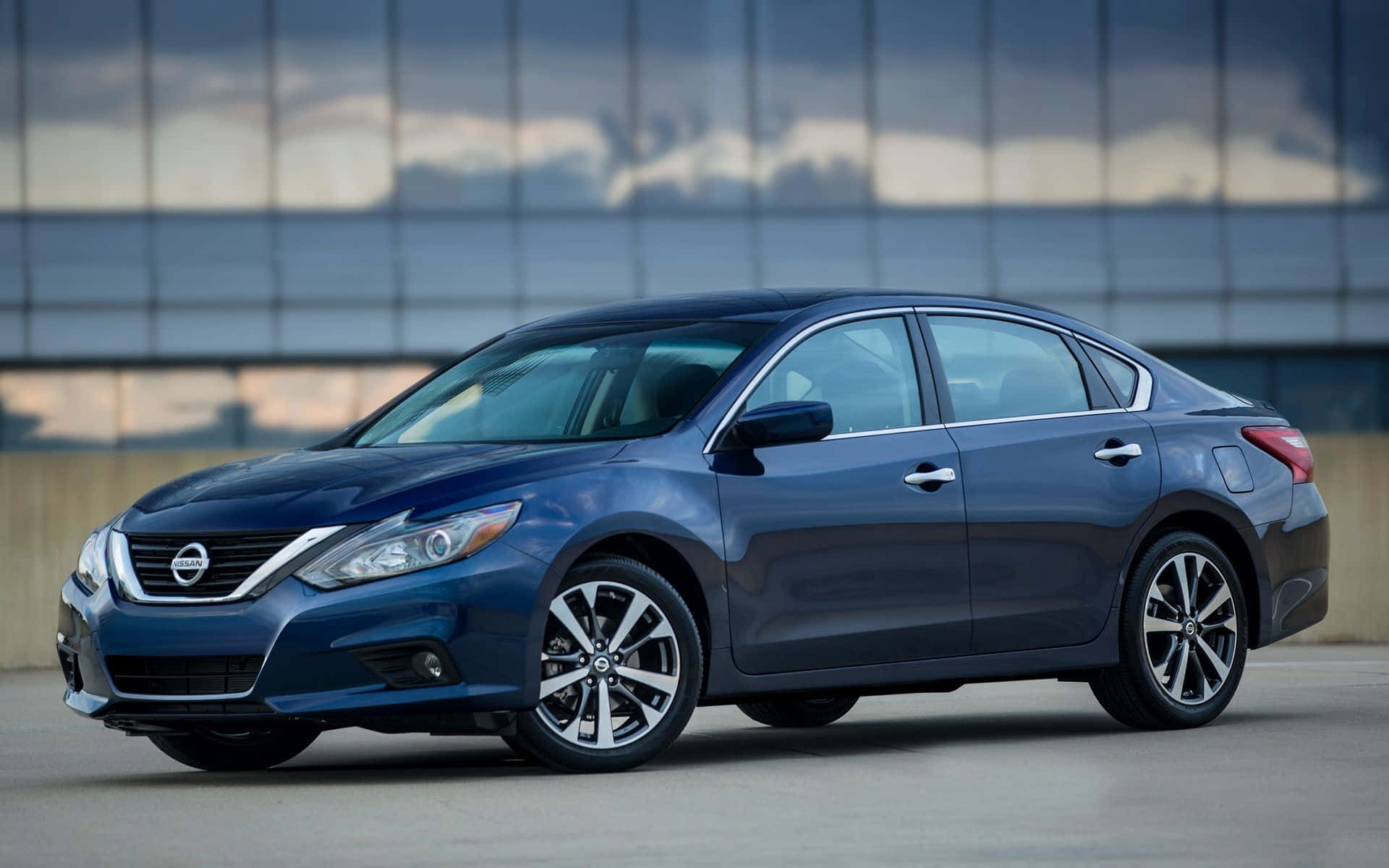Nissan Altima 桌布 壁紙 — 一輛時尚的藍色日產轎車停放在現代玻璃建築前，天空多雲。