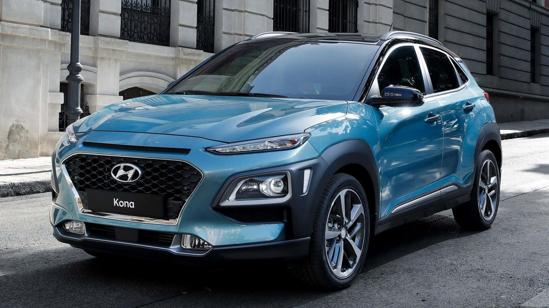 Hyundai Kona 桌布 壁紙 — 一輛時尚的藍色現代Kona SUV停泊在城市的街道上，背景是歷史悠久的石建築。