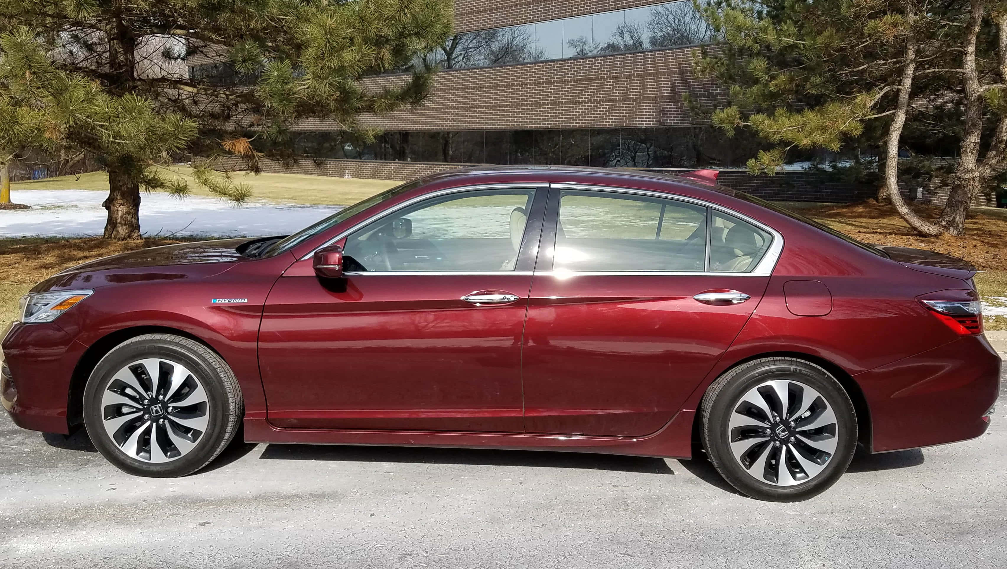 Honda Accord 桌布 壁紙 — 一輛時尚的栗色轎車停在雪地車道上，旁邊有松樹和現代磚砌建築。