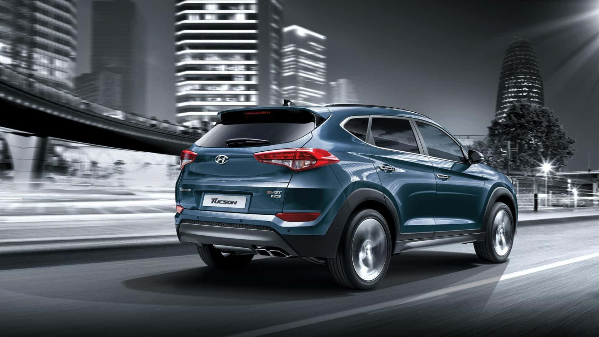 Hyundai Tucson 桌布 壁紙 — 一輛時尚的青綠色現代 Tucson SUV 在模糊的夜間城市景觀中疾馳，周圍是閃爍的摩天大樓。