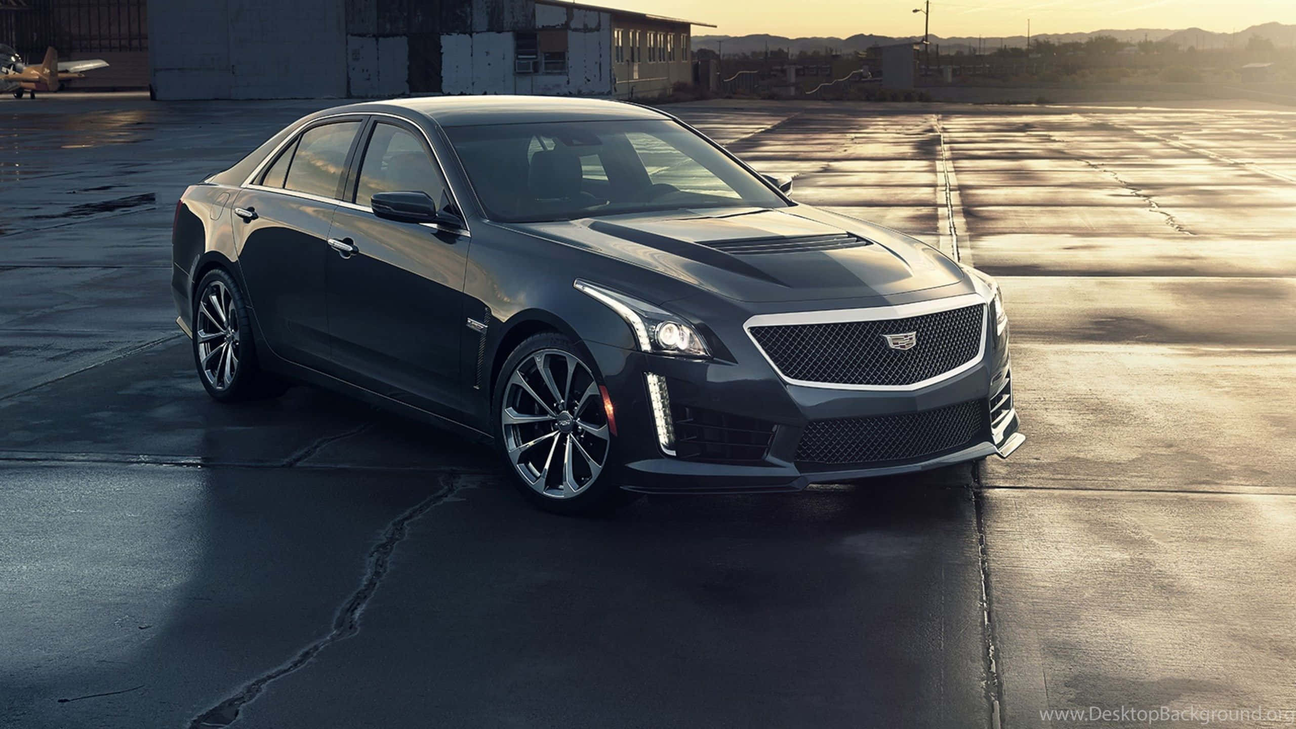 Cadillac Cts 桌布 壁紙 — 一輛時尚的深灰色凱迪拉克CTS-V轎車在金色時刻的光線下，在裂開的混凝土停機坪上閃閃發光。