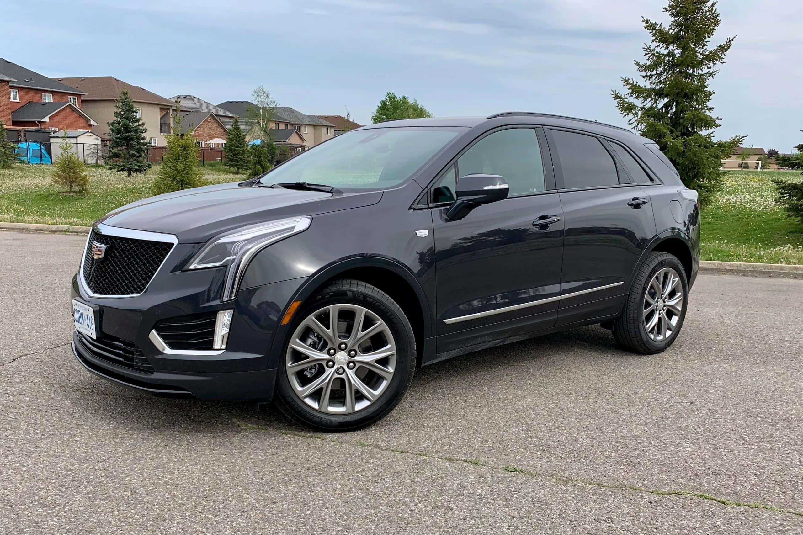 Cadillac Xt5 桌布 壁紙 — 一輛時尚的深灰色凱迪拉克 XT5 SUV 停泊在郊區街道上，背景有房屋和綠樹。