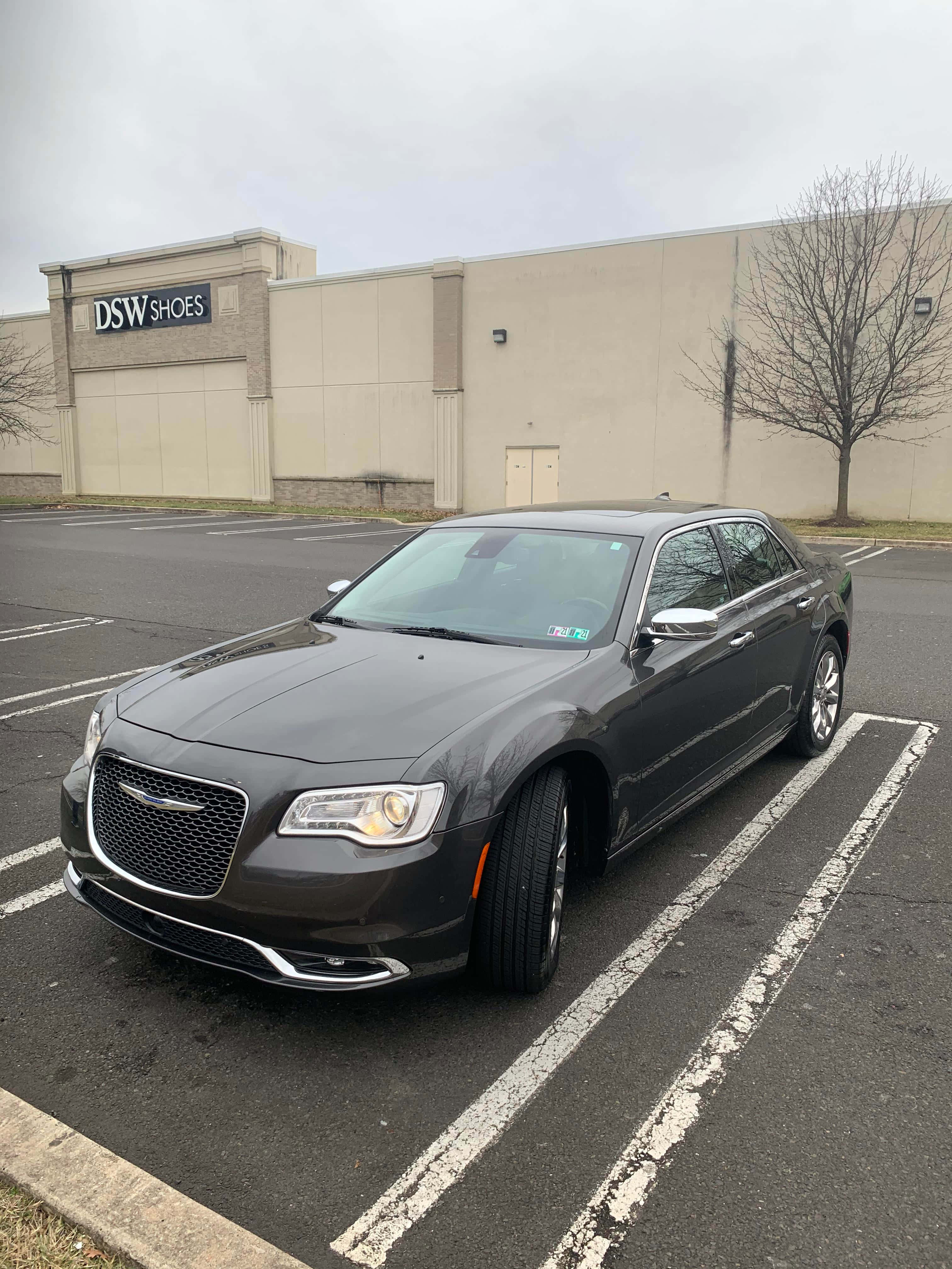 Chrysler 300 桌布 壁紙 — 一輛時尚的深灰色克萊斯勒轎車停在濕漉漉的停車場，背景是DSW Shoes商店，天空多雲。