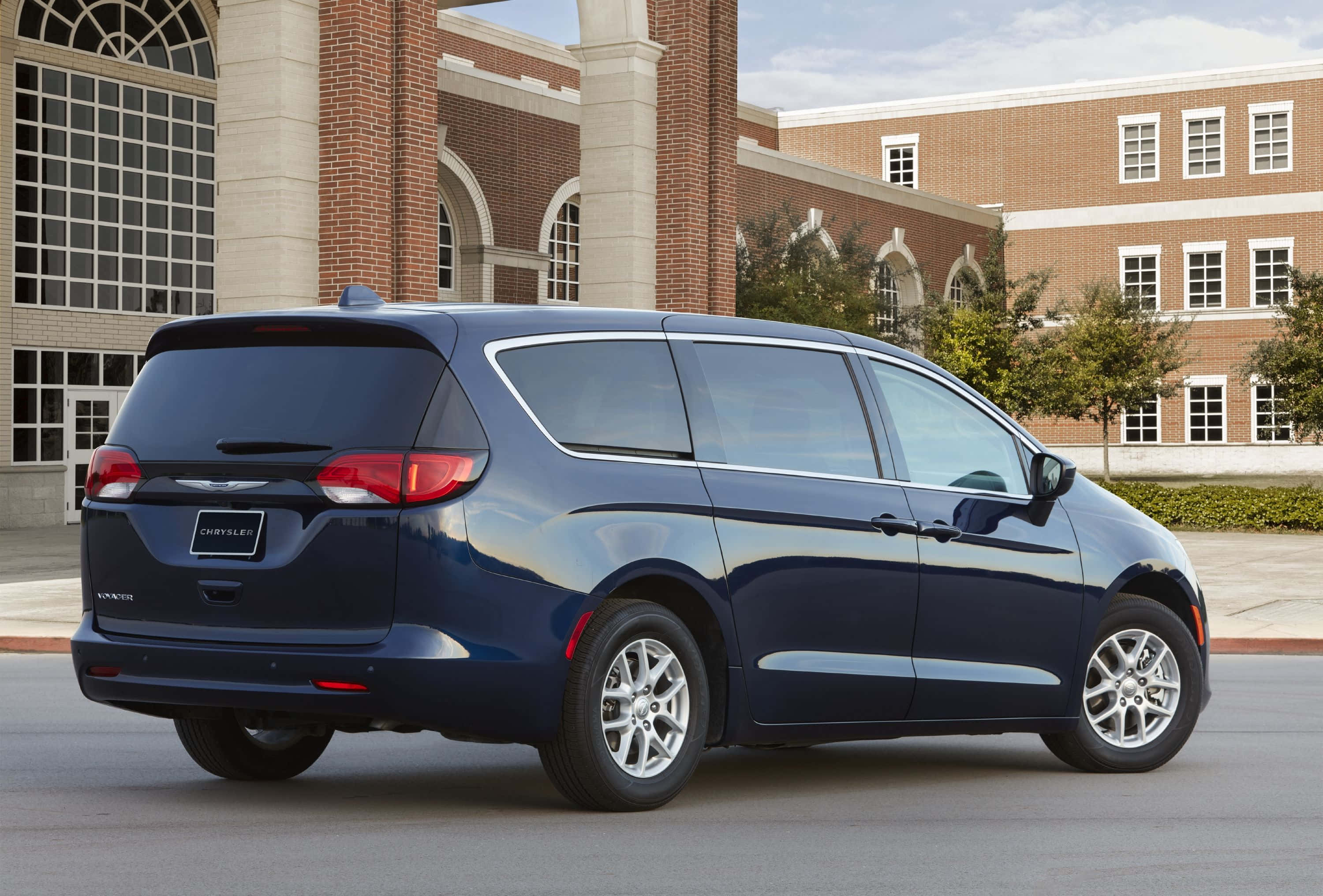 Chrysler Voyager 桌布 壁紙 — 一輛時尚的深藍色 Chrysler Pacifica 小型貨車停在有拱形窗戶的磚砌建築前。