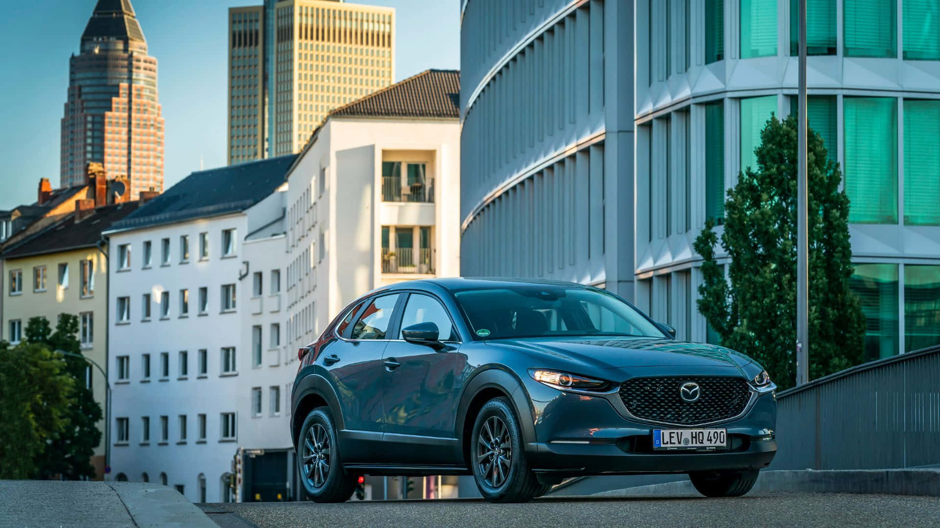 Mazda Cx-3 桌布 壁紙 — 一輛時尚的深藍色Mazda CX-3停放在現代與歷史建築交錯的城市街道上，天空晴朗。