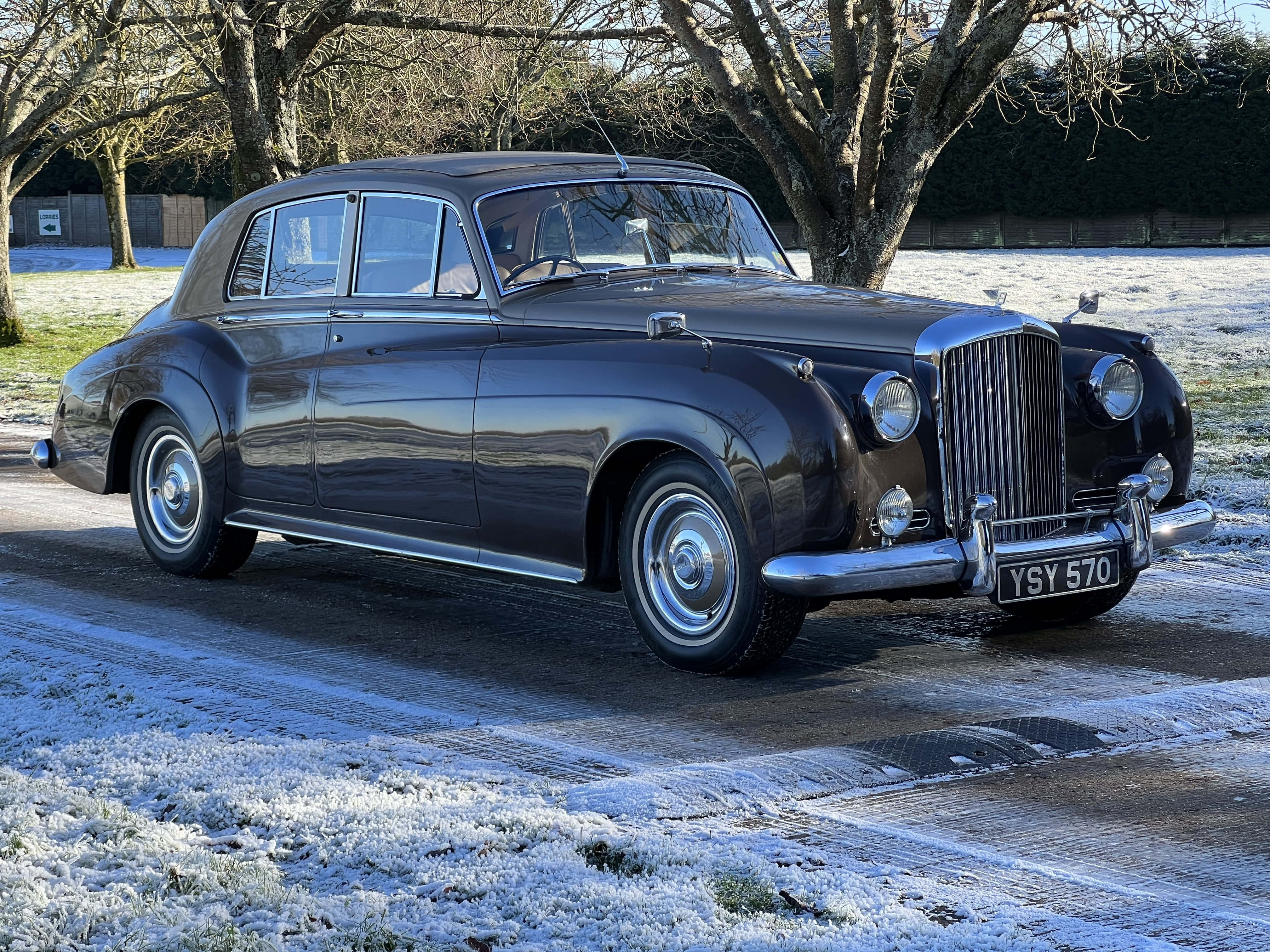 Bentley S2 桌布 壁紙 — 一輛時尚的 vintage Bentley 轎車在冬日陽光下，在鋪滿霜的車道上，在光禿禿的樹旁邊閃閃發光。
