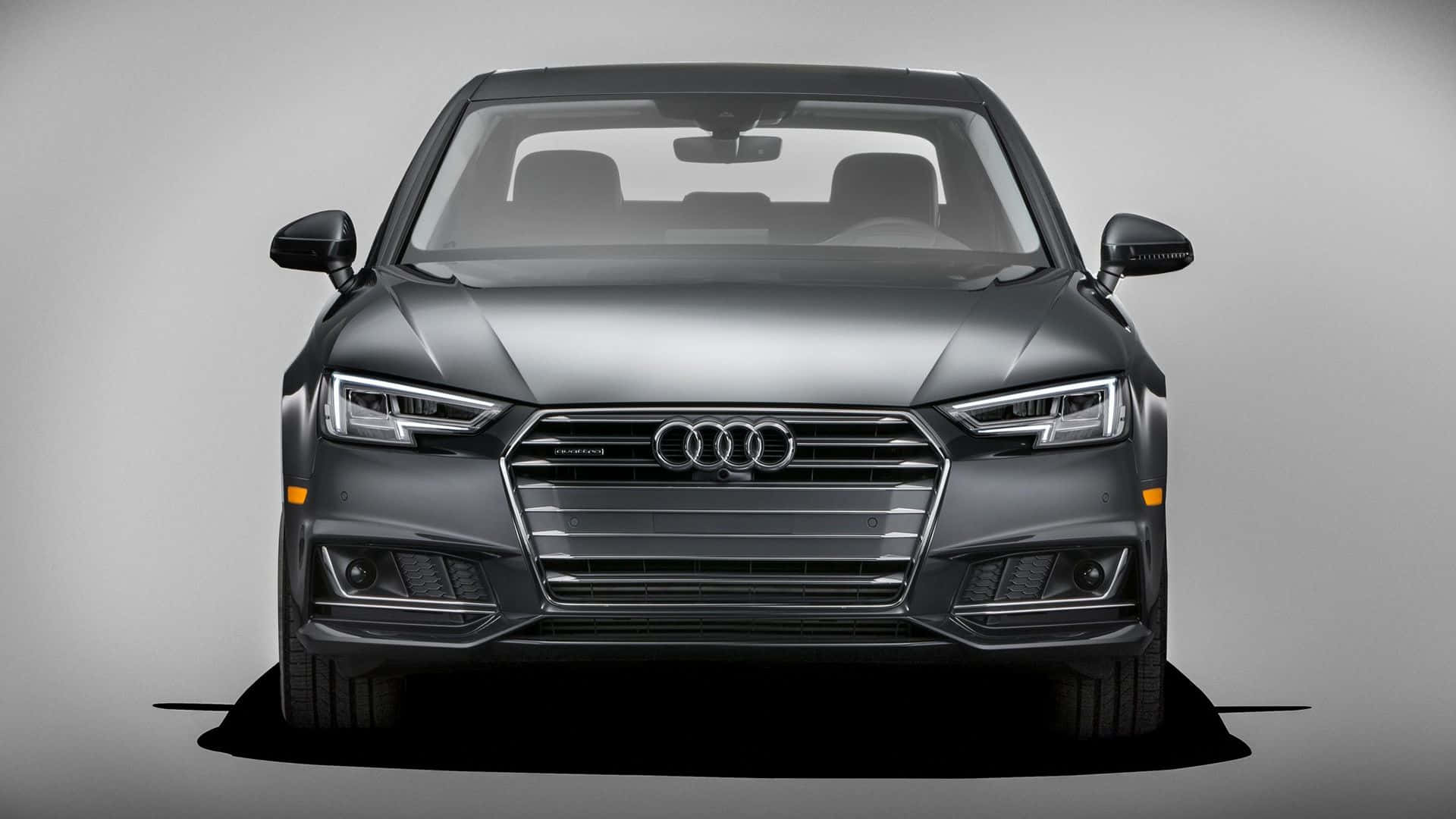 Audi A4 桌布 壁紙 — 一輛時尚的消光灰色奧迪轎車正面視圖，配備銳利頭燈和鍍鉻水箱護罩，背景為中性攝影棚。