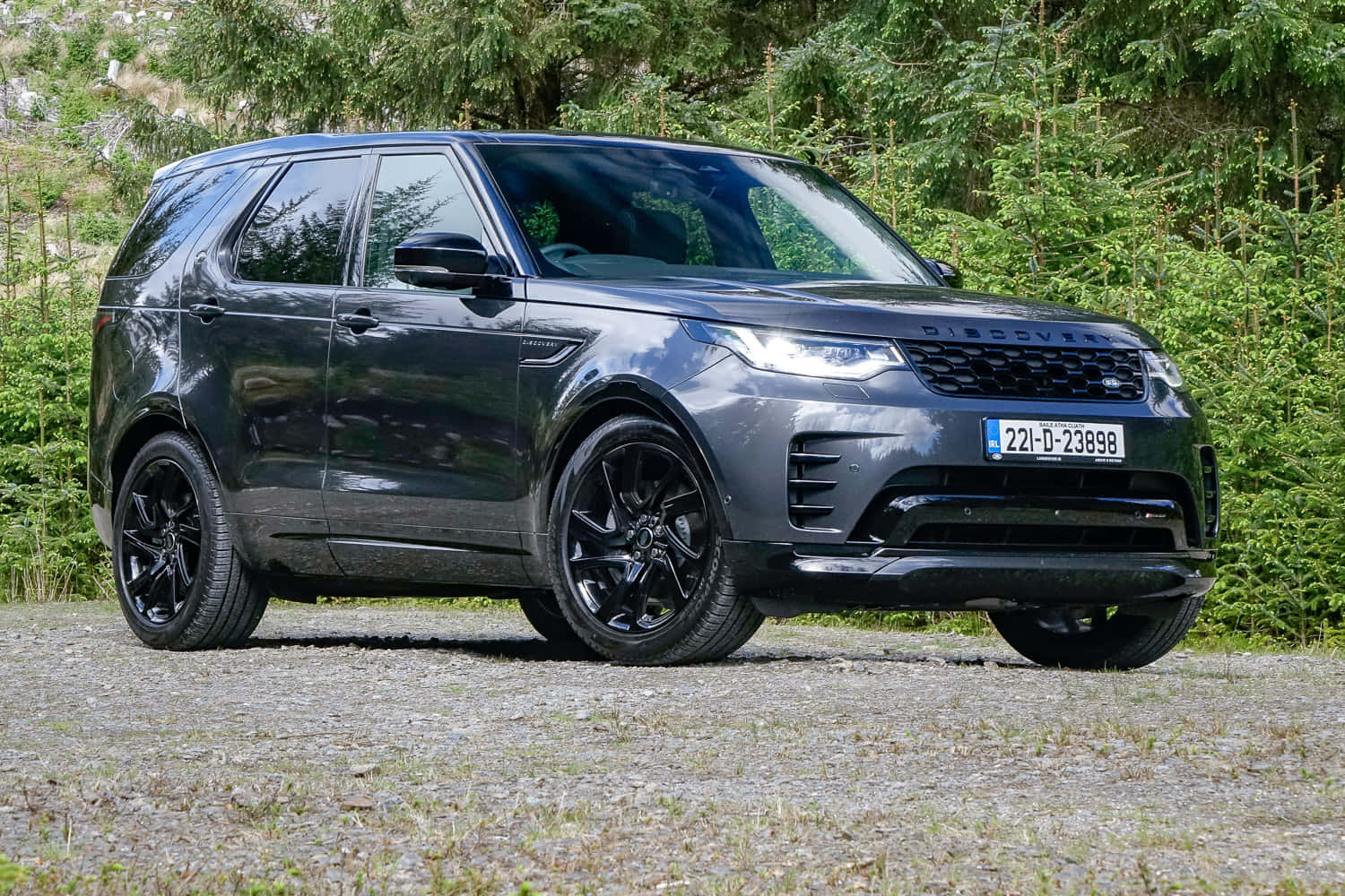 Land Rover Discovery 桌布 壁紙 — 一輛時尚的啞光灰色 Land Rover Discovery 停在碎石路上，背後是茂密的綠色森林。