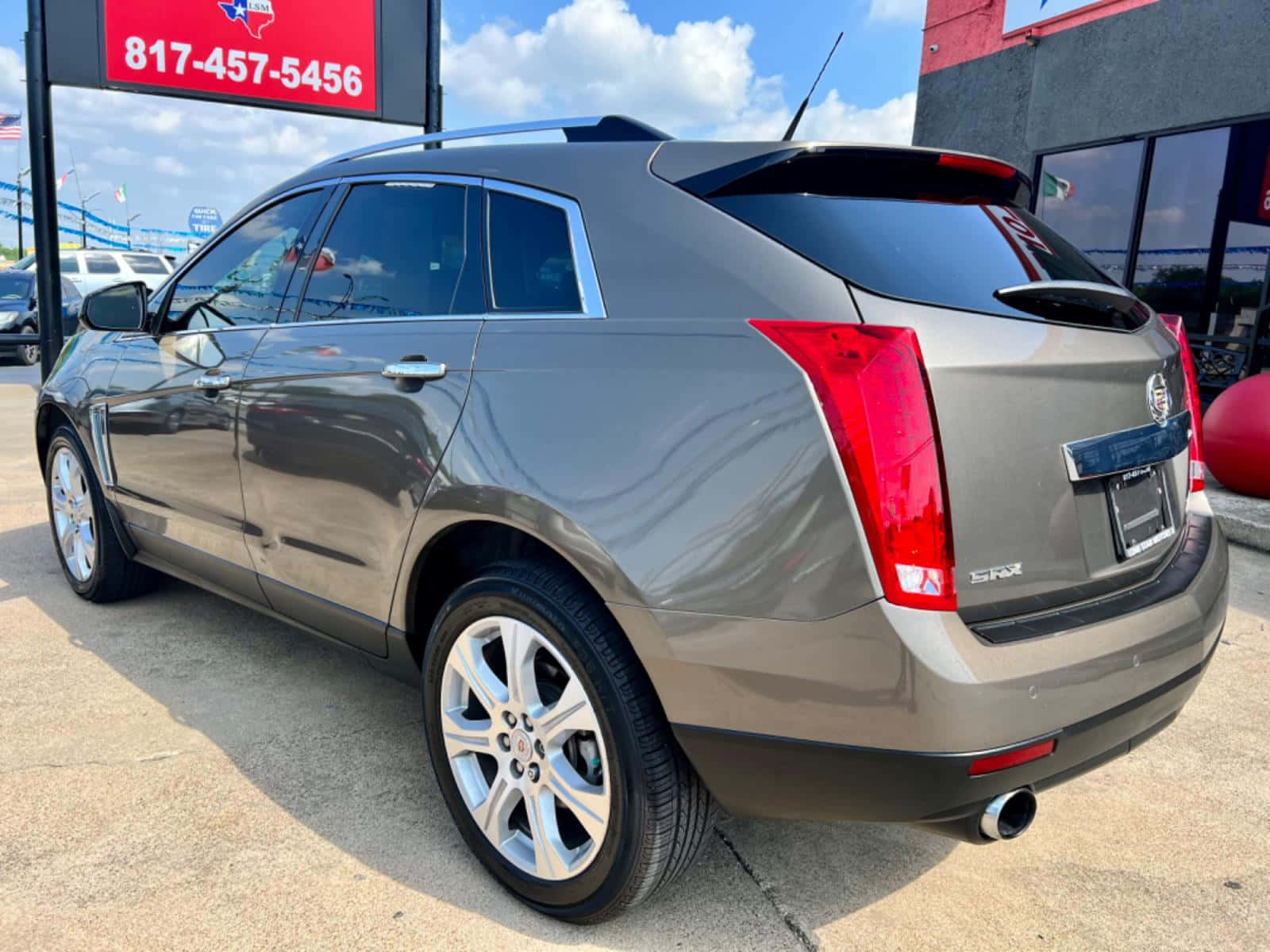 Cadillac Srx 桌布 壁紙 — 一輛時尚的銀灰色Cadillac SRX SUV停放在戶外，天空湛藍，白雲點綴。