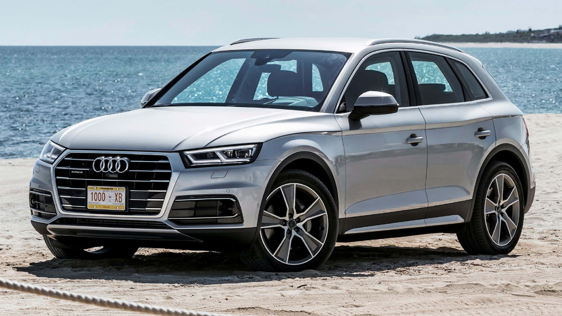 Audi Q5 桌布 壁紙 — 一輛時尚的銀色奧迪Q5 SUV停泊在沙灘上，背後有海浪和清澈的藍天。