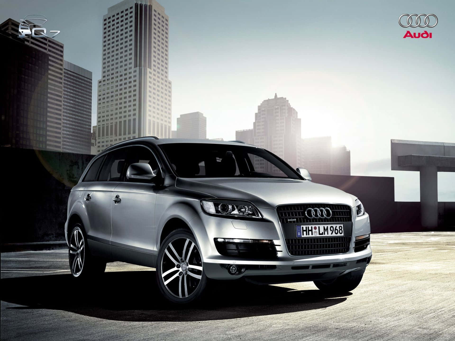 Audi Q7 桌布 壁紙 — 一輛時尚的銀色 Audi Q7 SUV 停泊在屋頂上，現代城市天際線在柔和的晨光中閃耀。