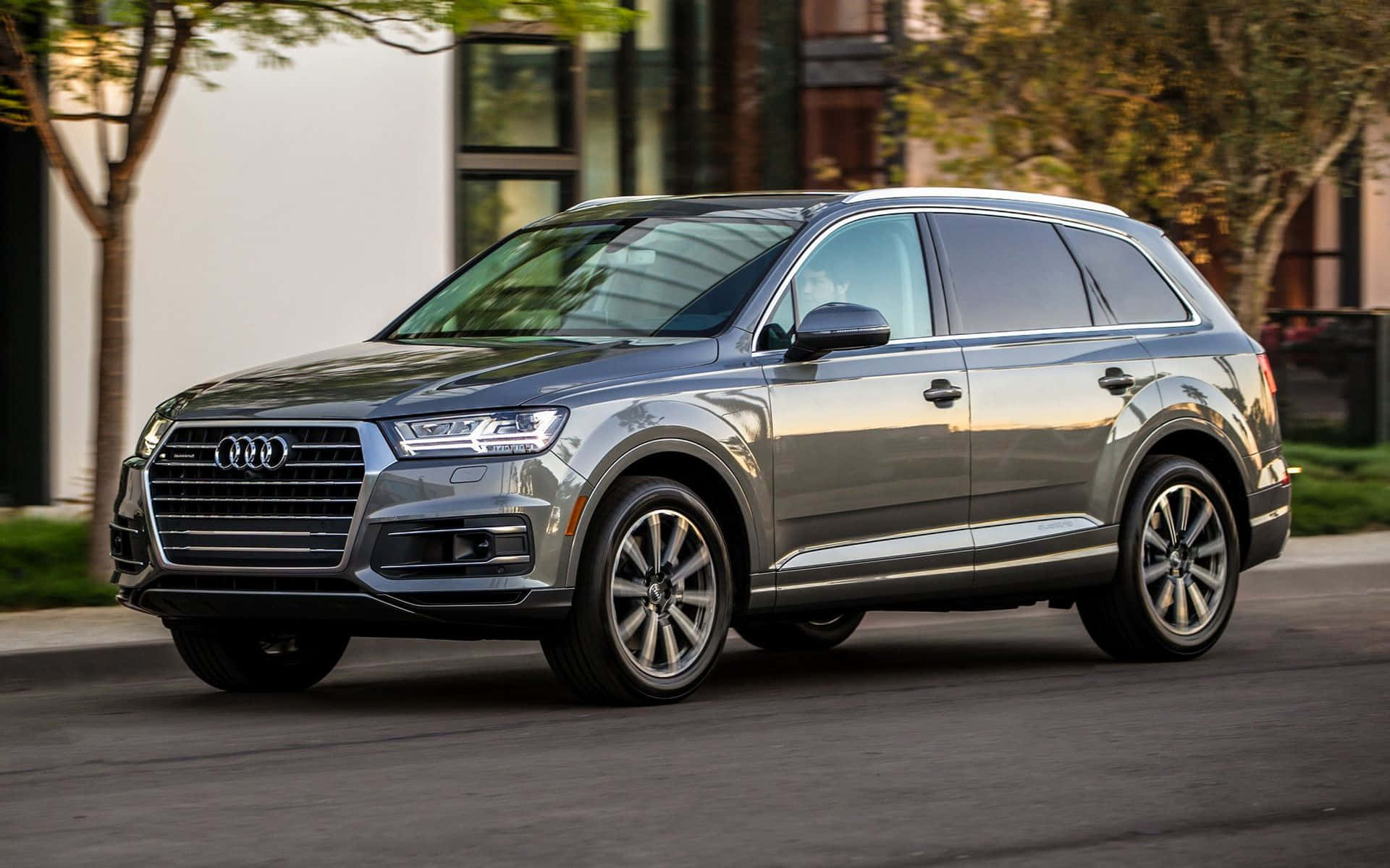 Audi Q7 桌布 壁紙 — 一輛時尚的銀色Audi Q7 SUV停放在城市的街道上，背景是現代建築和樹木。