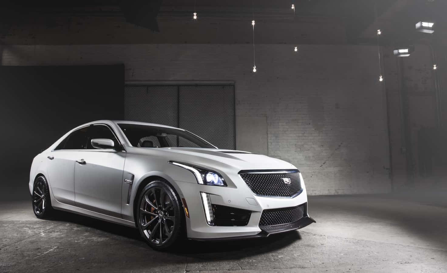 Cadillac Ats 桌布 壁紙 — 一輛時尚的銀色Cadillac ATS-V轎跑車在粗獷的工業倉庫中，在戲劇性的攝影棚燈光下閃閃發光。