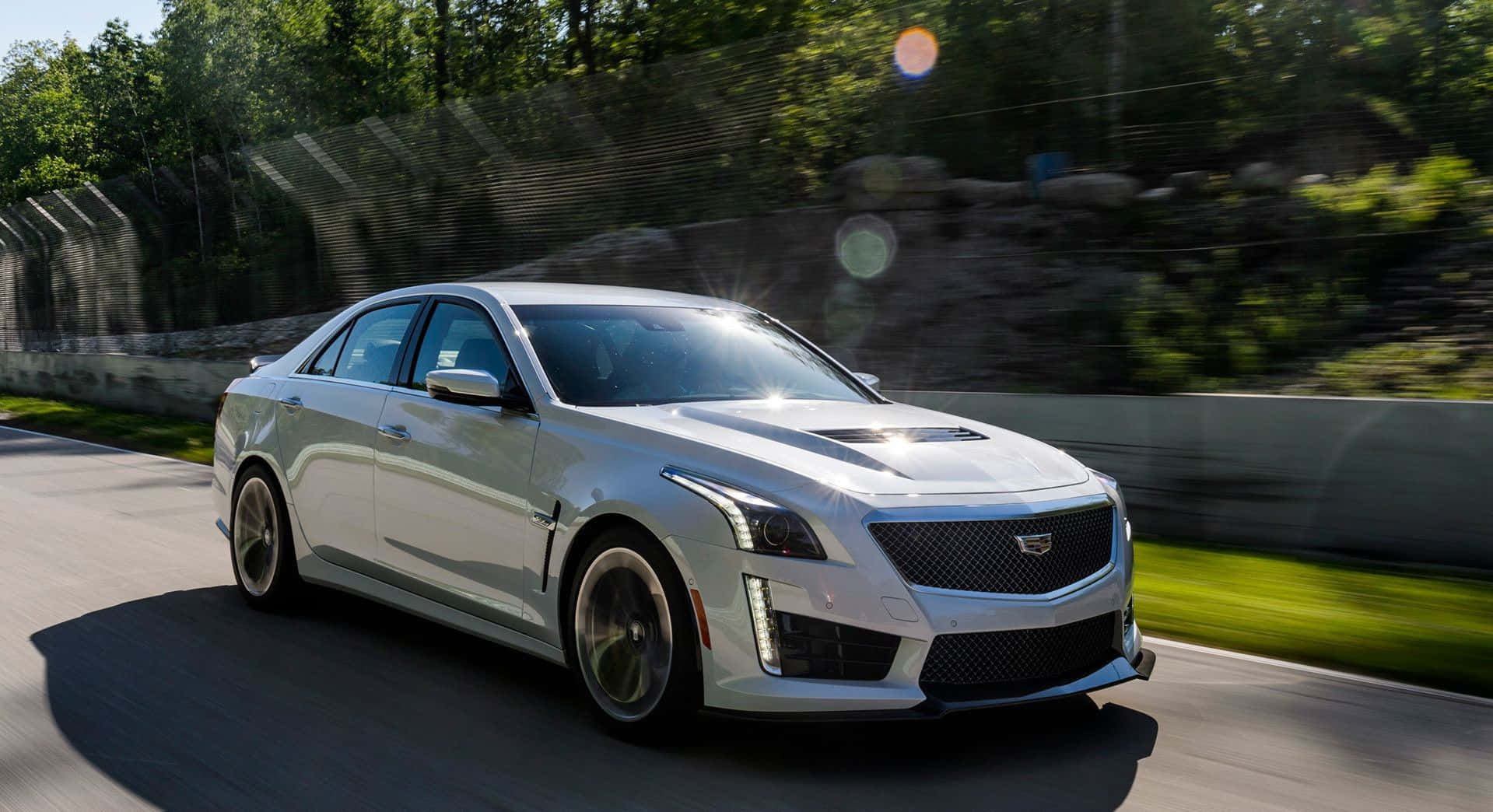 Cadillac Cts 桌布 壁紙 — 一輛時尚的銀色Cadillac CTS-V在陽光明媚的賽道上疾馳，背景是模糊的綠化和石牆。