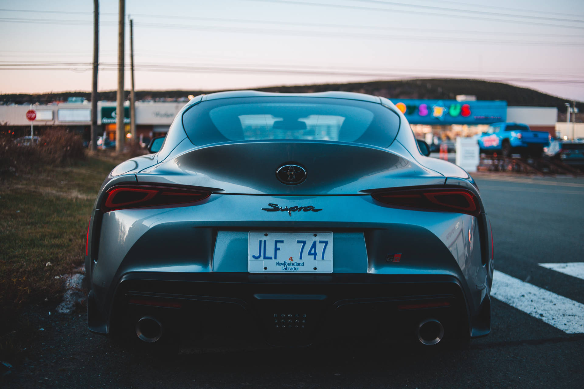 銀色豐田Supra在黃昏時停泊在街上，後面有霓虹燈牌。 — Toyota Supra 壁紙
