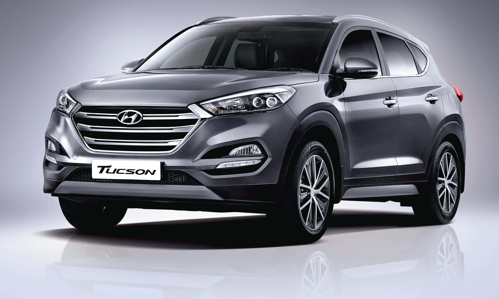 Hyundai Tucson 桌布 壁紙 — 一輛時尚的銀色Hyundai Tucson SUV在設有反射地板和漸變灰色背景的攝影棚中展示。