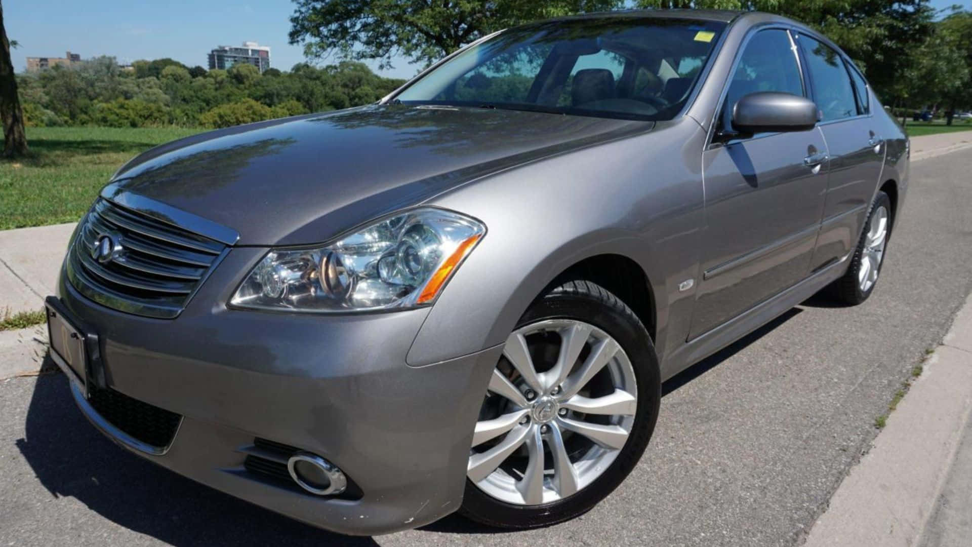 Infiniti M35 桌布 壁紙 — 一輛時尚的銀色Infiniti轎車停放在陽光明媚的街道上，背景有綠樹和建築物。