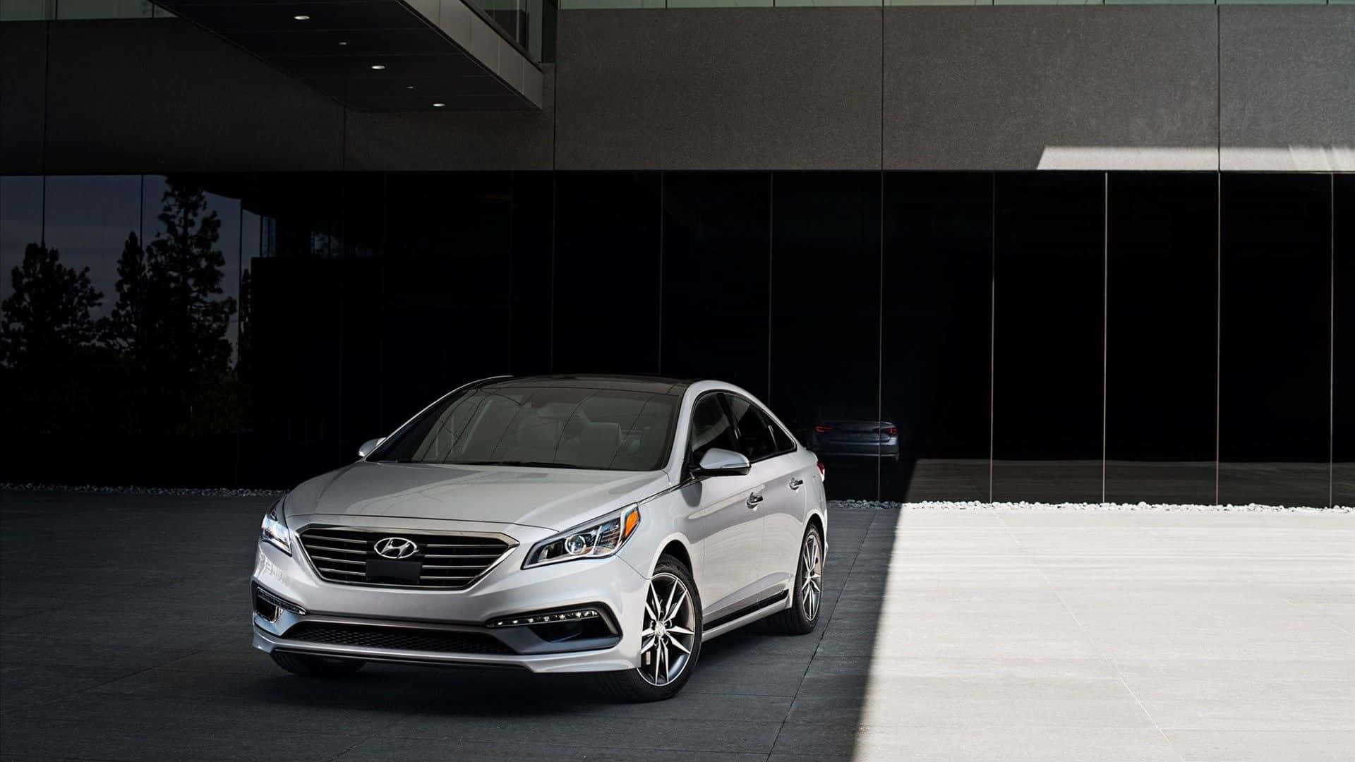 Hyundai Sonata 桌布 壁紙 — 一輛時尚的銀色轎車停在一棟現代玻璃建築前，燈光效果戲劇化。