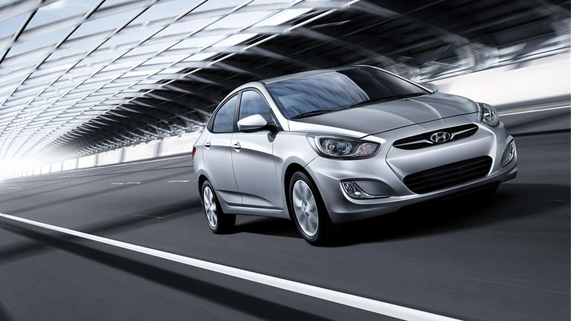 Hyundai Accent 桌布 壁紙 — 一輛時尚的銀色轎車在現代玻璃隧道中高速行駛，動態模糊強調了速度。
