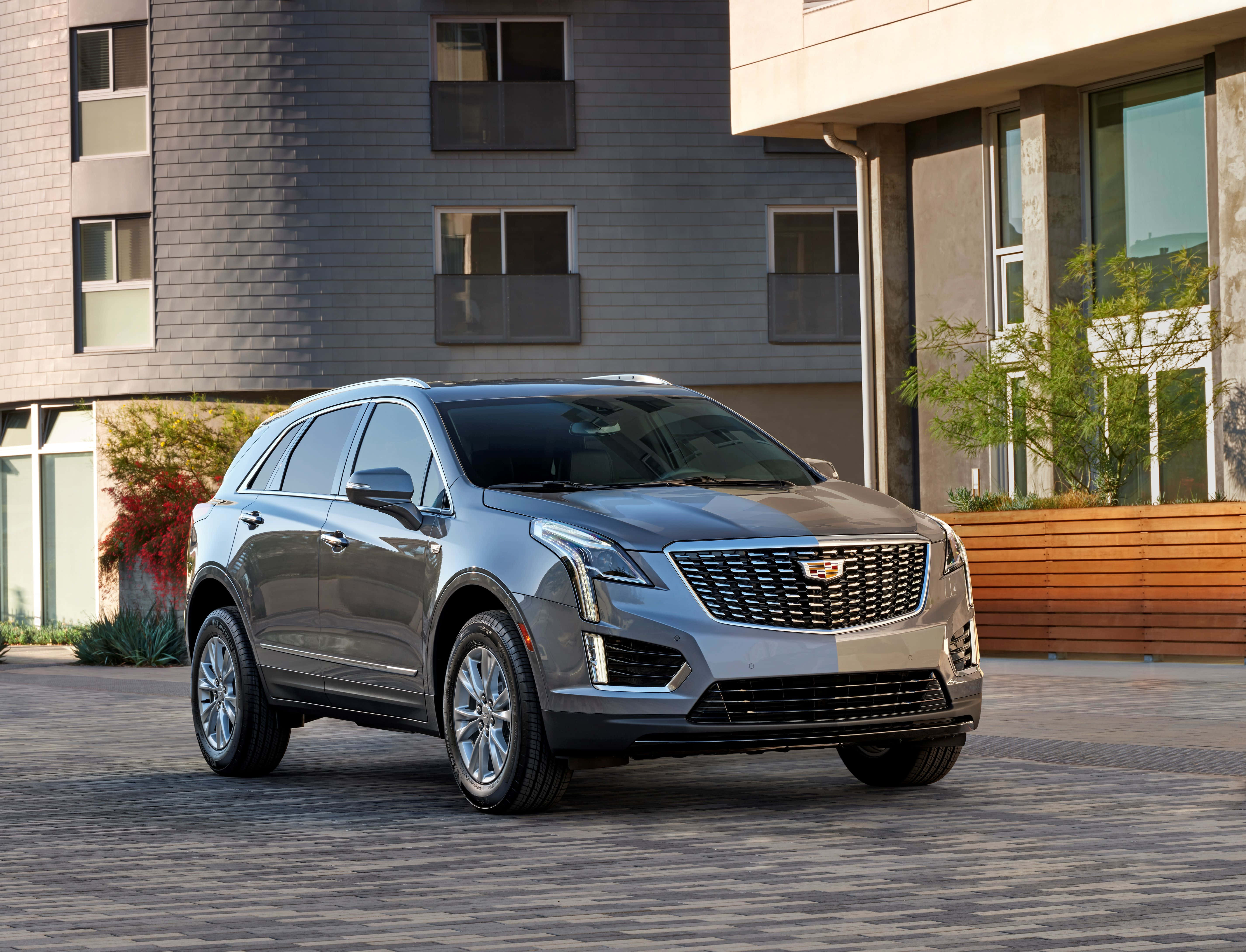 Cadillac Xt5 桌布 壁紙 — 一輛時尚的銀色凱迪拉克SUV停放在鋪砌的庭院中，前面是一座帶有灰色牆板和木質裝飾的現代建築。
