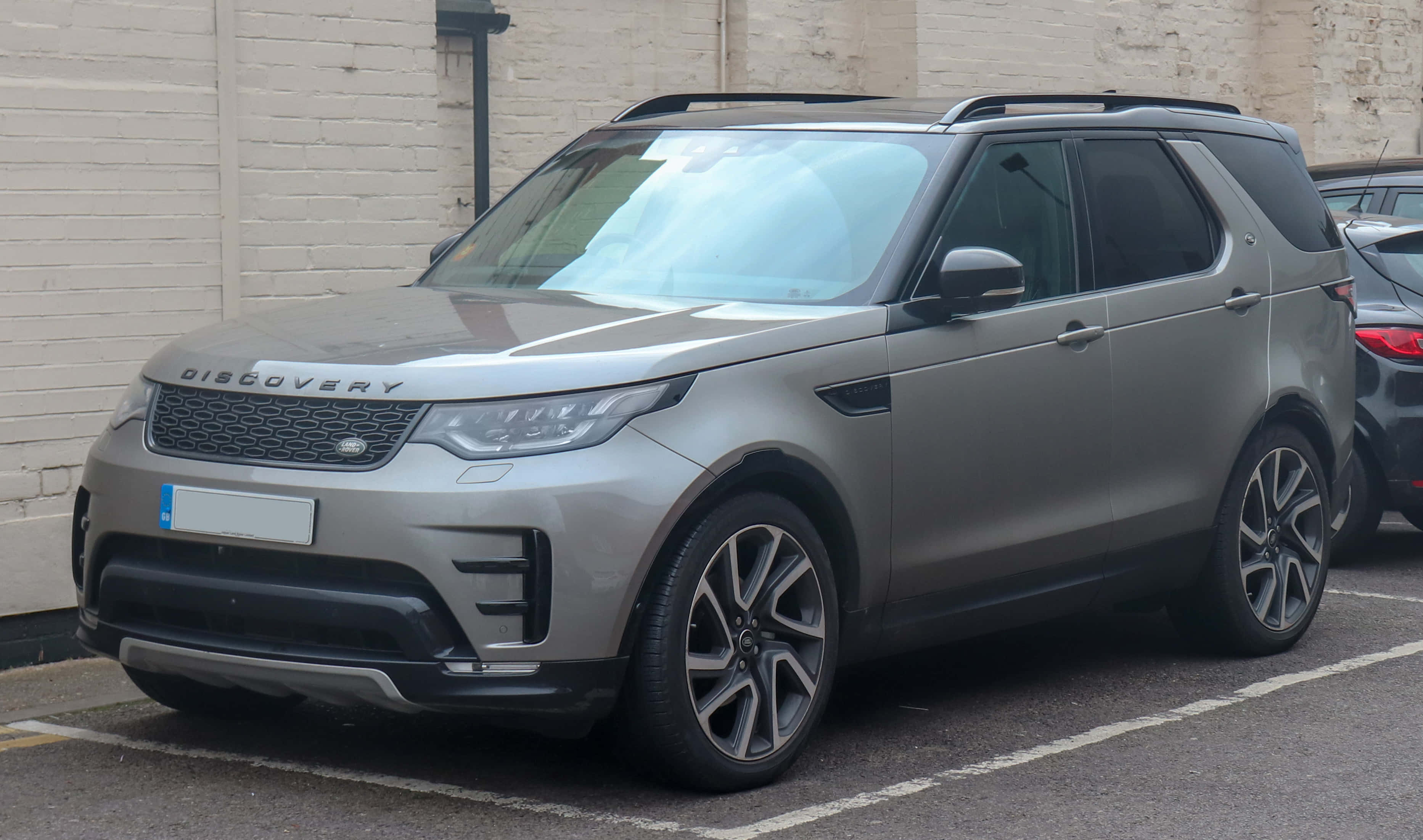 Land Rover Discovery 桌布 壁紙 — 一輛時尚的銀色 Land Rover Discovery SUV 停放在城市地塊旁邊的白色磚牆旁。