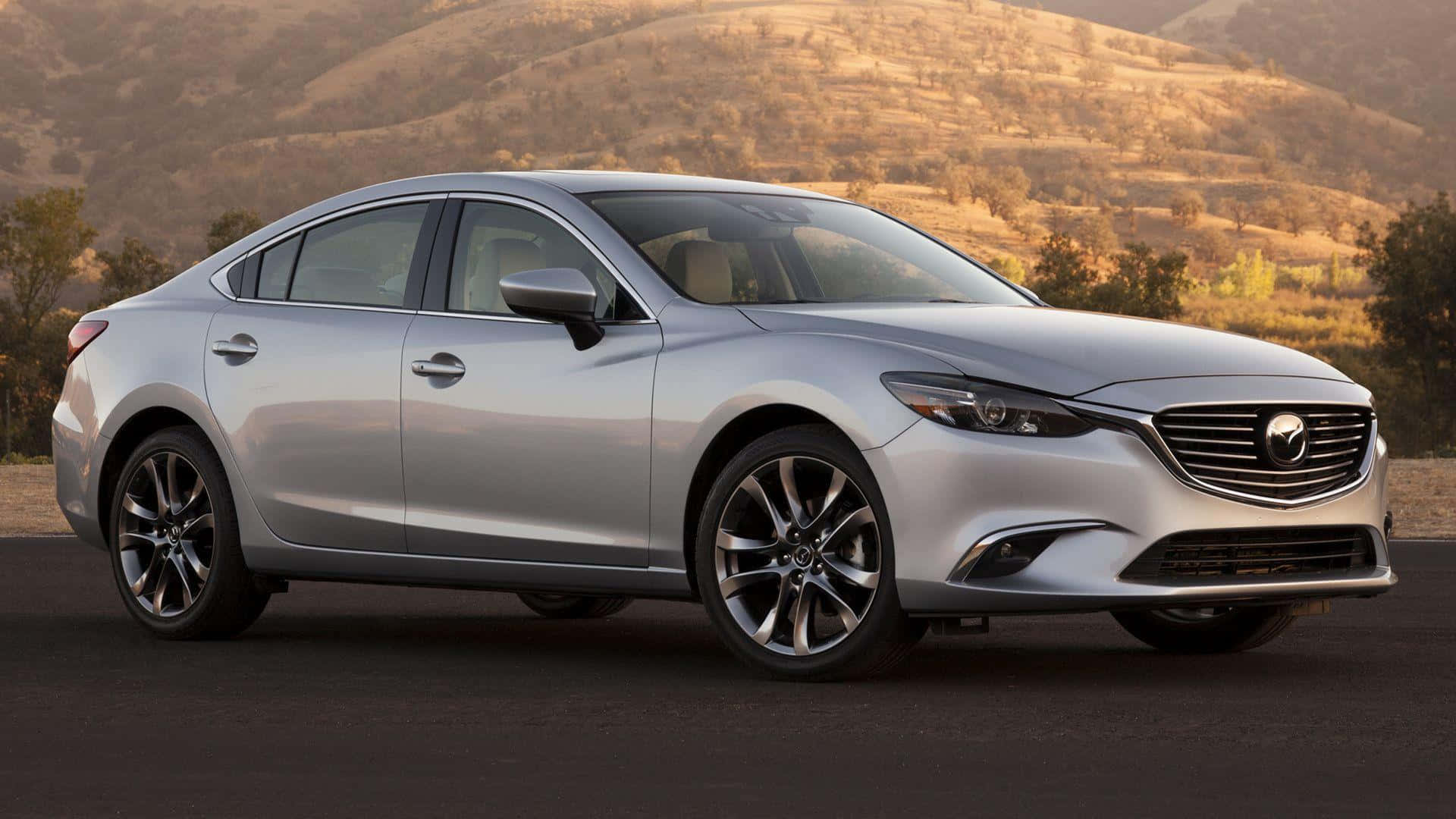 Mazda 6 桌布 壁紙 — 一輛時尚的銀色Mazda6轎車停在柏油路上，背景是溫暖陽光下的金色起伏山丘和稀疏樹木。