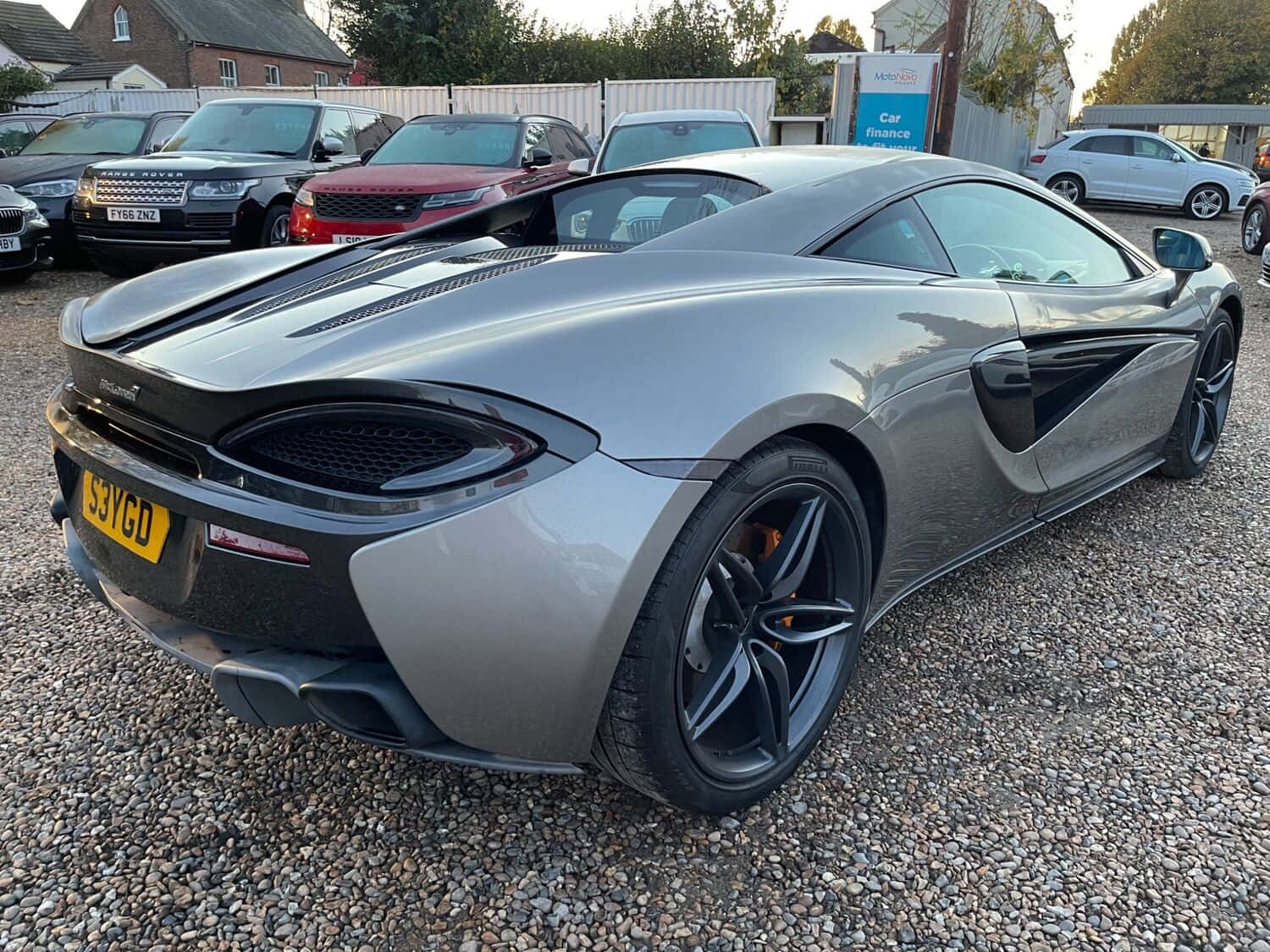Mclaren 540c 桌布 壁紙 — 一輛時尚的銀色McLaren 570S跑車停放在碎石地上，背景有其他車輛。